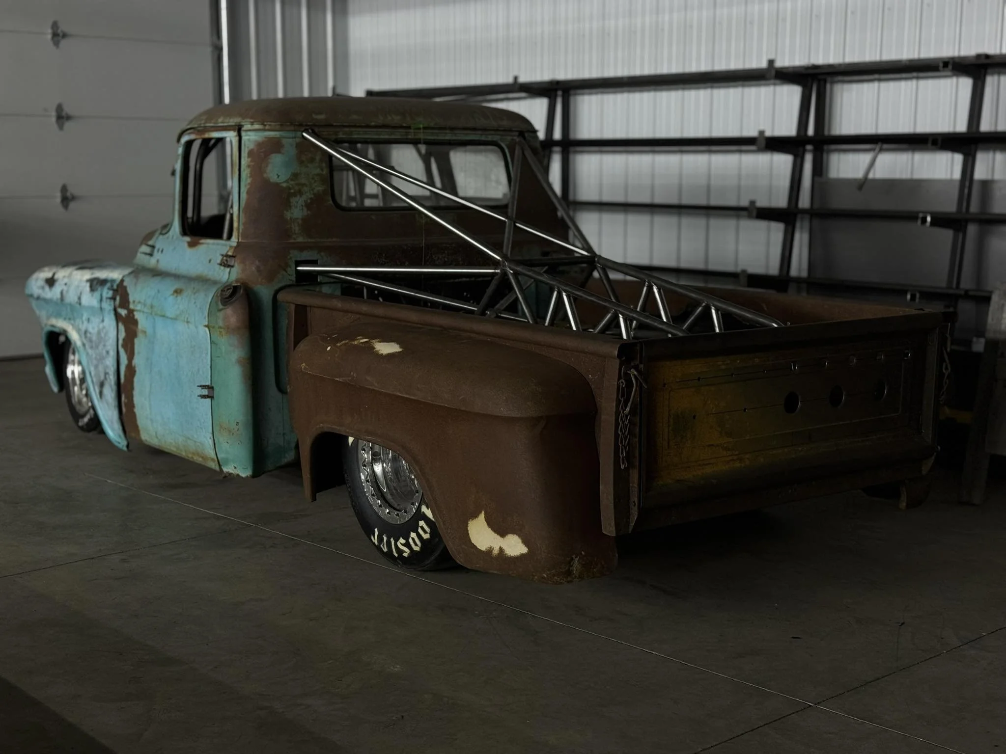 Old rusted pickup truck with a blue and brown body, interior bed filled with a metal truss framework, inside a storage garage.