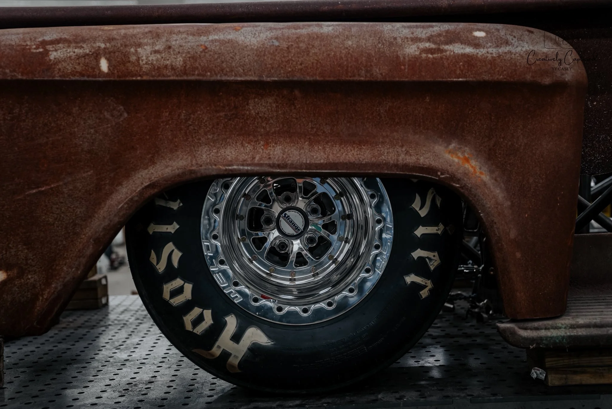 Close-up of a vintage car's rusty exterior with a shiny, custom metal wheel and tire.