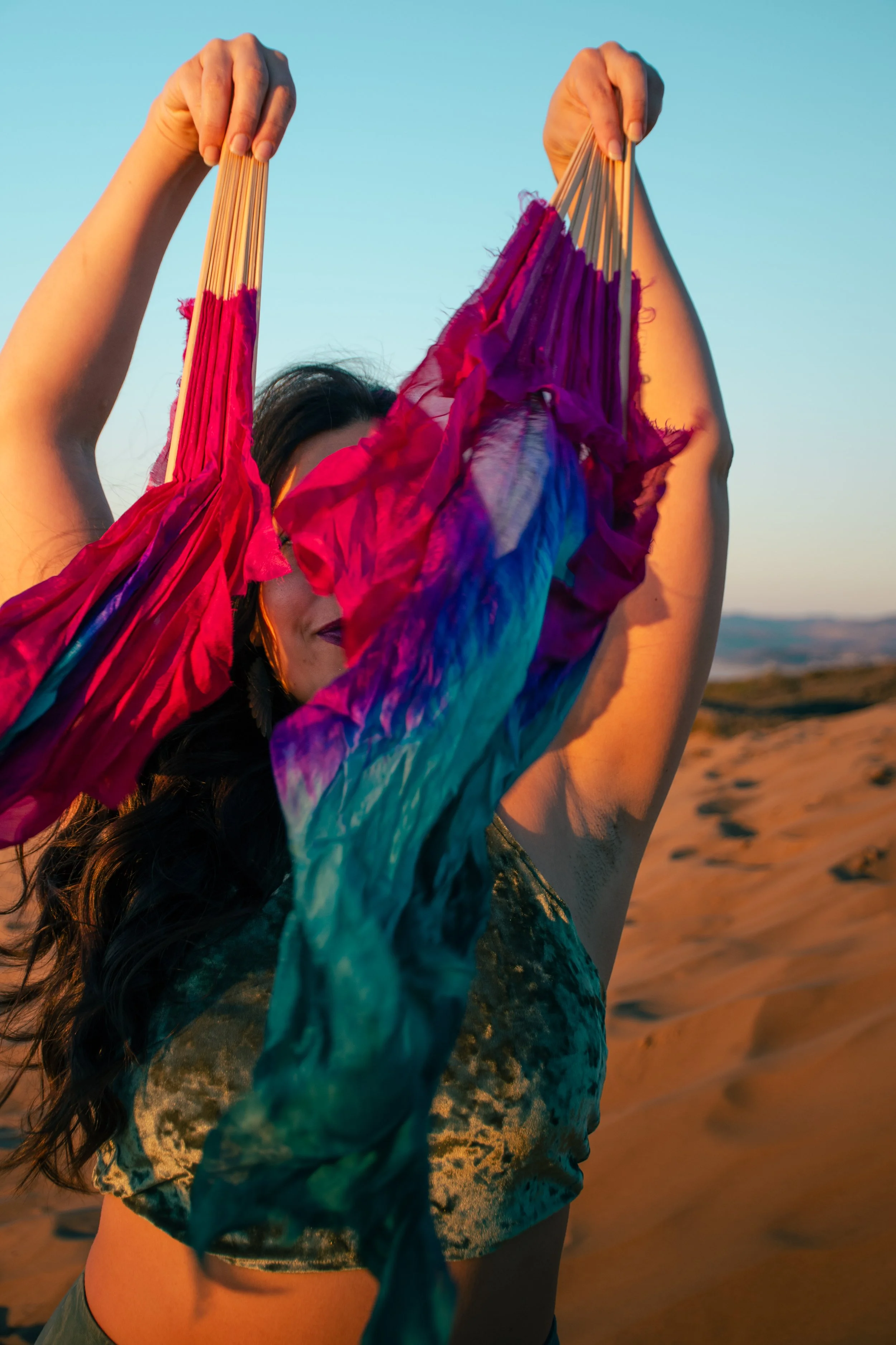 A woman holding colorful fabric or scarf up in a desert landscape during sunset.