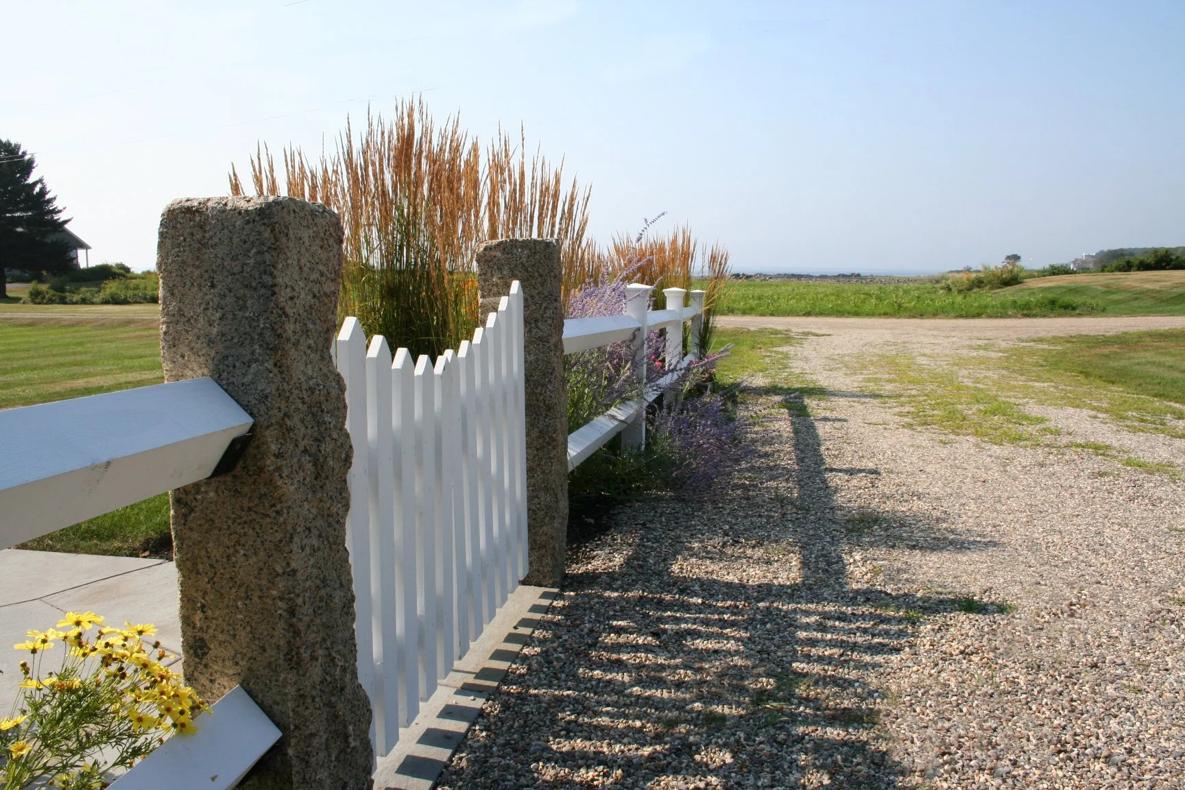 Seabreeze Cottage features a charming white picket fence, lush coastal plantings, and a welcoming New England landscape designed to enhance curb appeal and outdoor living. This timeless residential landscape by Sea Laurel Landscape Architecture blend
