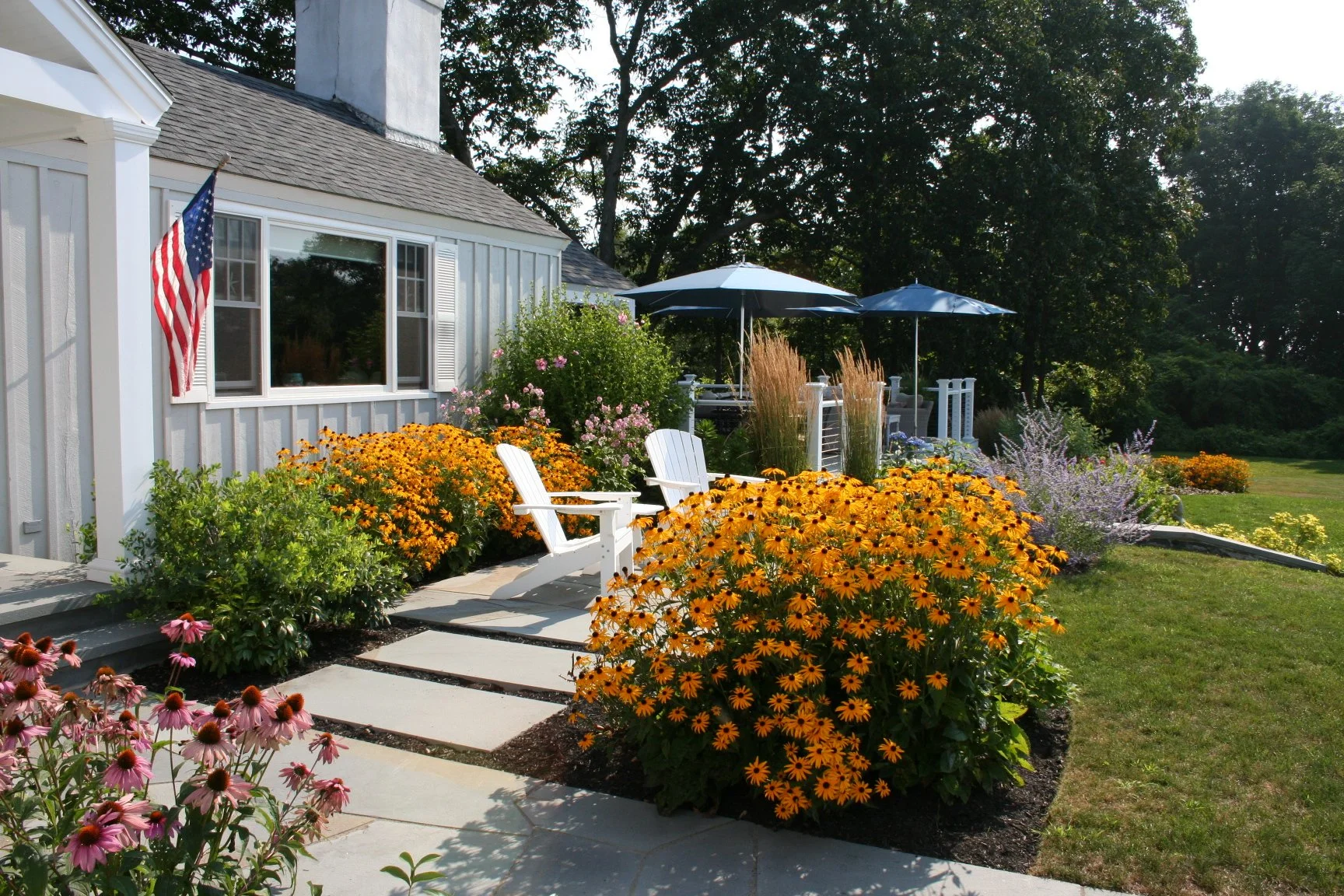 Seabreeze Cottage features a charming white picket fence, lush coastal plantings, and a welcoming New England landscape designed to enhance curb appeal and outdoor living. This timeless residential landscape by Sea Laurel Landscape Architecture blend