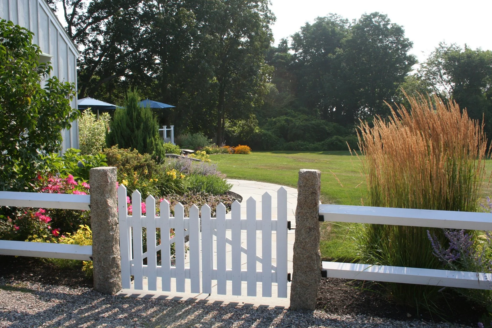 Seabreeze Cottage features a charming white picket fence, lush coastal plantings, and a welcoming New England landscape designed to enhance curb appeal and outdoor living. This timeless residential landscape by Sea Laurel Landscape Architecture blend