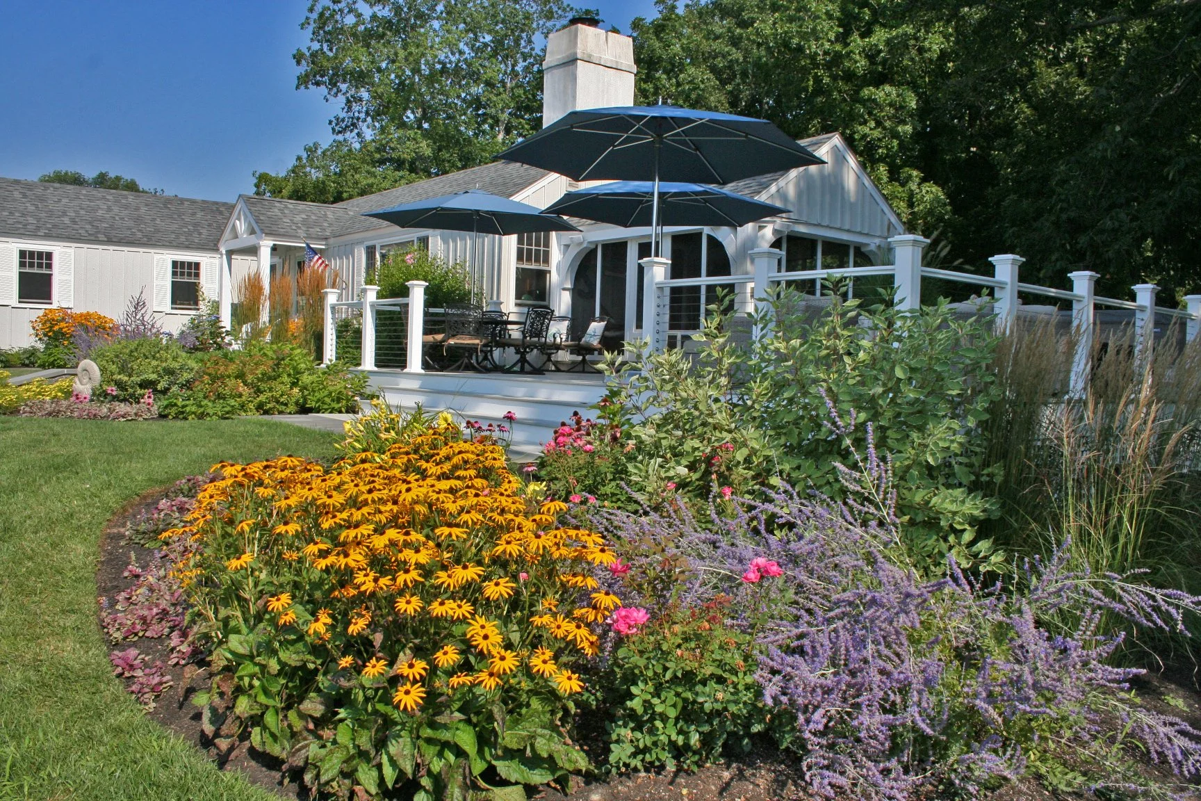 Seabreeze Cottage features a charming white picket fence, lush coastal plantings, and a welcoming New England landscape designed to enhance curb appeal and outdoor living. This timeless residential landscape by Sea Laurel Landscape Architecture blend