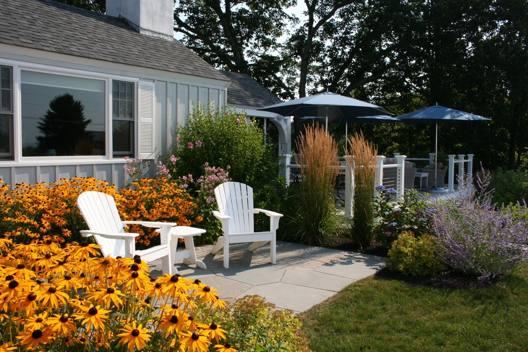 Seabreeze Cottage features a charming white picket fence, lush coastal plantings, and a welcoming New England landscape designed to enhance curb appeal and outdoor living. This timeless residential landscape by Sea Laurel Landscape Architecture blend