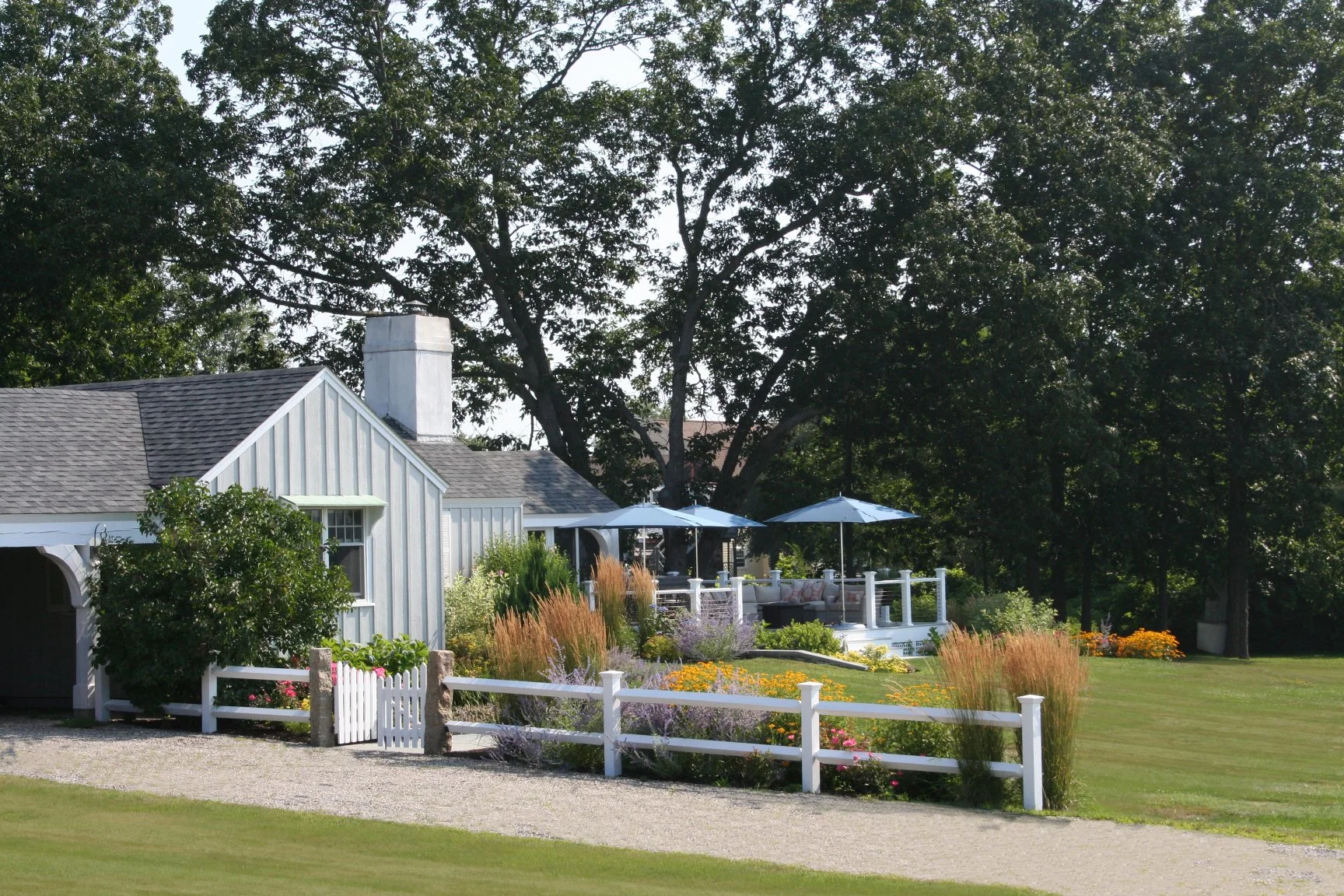 Seabreeze Cottage features a charming white picket fence, lush coastal plantings, and a welcoming New England landscape designed to enhance curb appeal and outdoor living. This timeless residential landscape by Sea Laurel Landscape Architecture blend