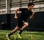 A man running through an agility drill with yellow hurdles in an indoor sports facility.