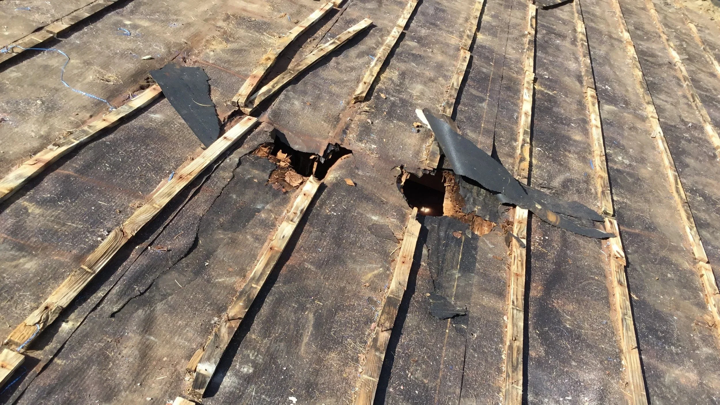 Rotted and damaged roof with holes during a tear-off showing wood beams.