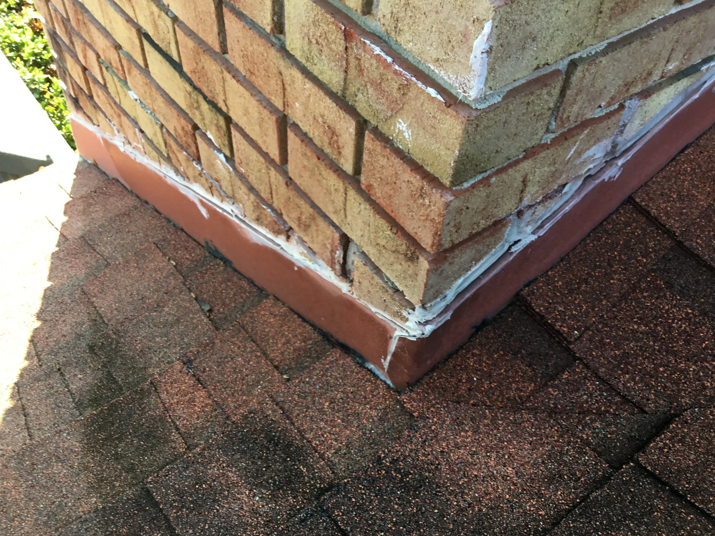 Chimney flashing detail showing a poor installation where caulking was used as the primary waterproofing — a method that almost always cracks, shrinks, and leaks within a few years. Proper chimney flashing requires layered metal step flashing integra