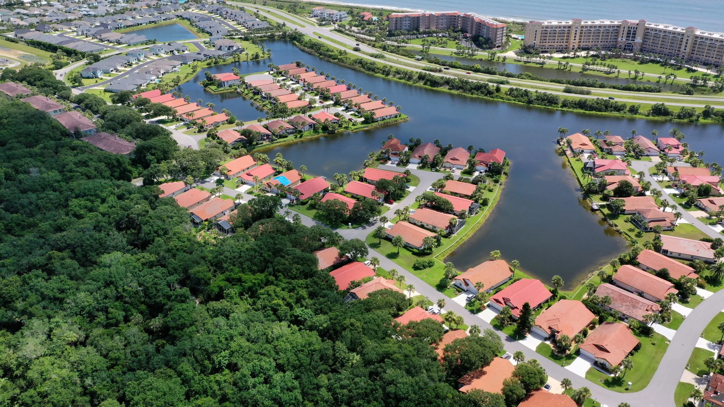 Aerial view of a residential neighborhood with houses, water bodies, and a large hotel or apartment complex nearby.