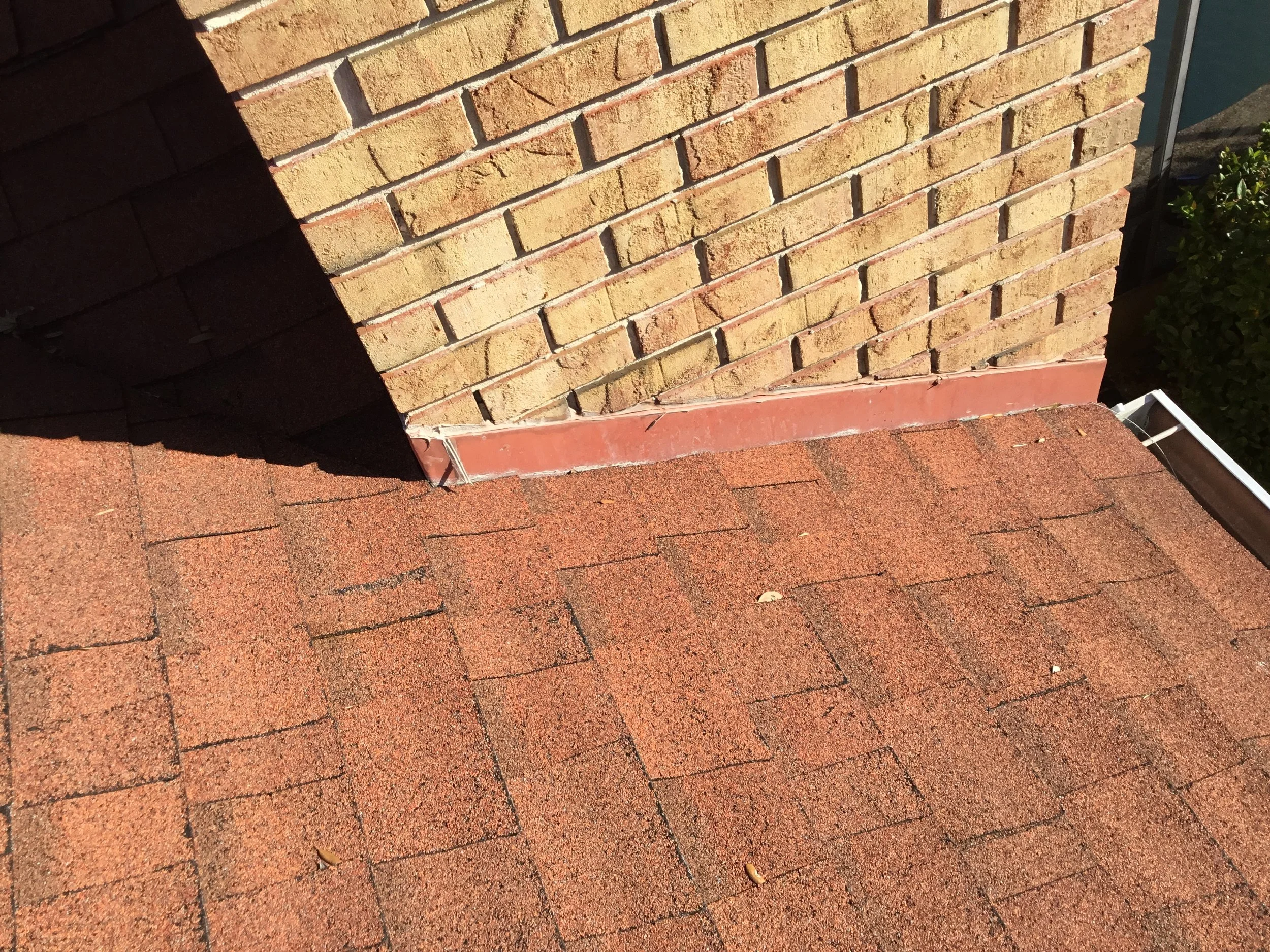Improper wall flashing at a roof-to-brick transition, where exposed metal and inadequate integration leave the joint vulnerable to water intrusion. When flashing isn’t correctly layered behind the wall and tied into the shingles, rain can track behin