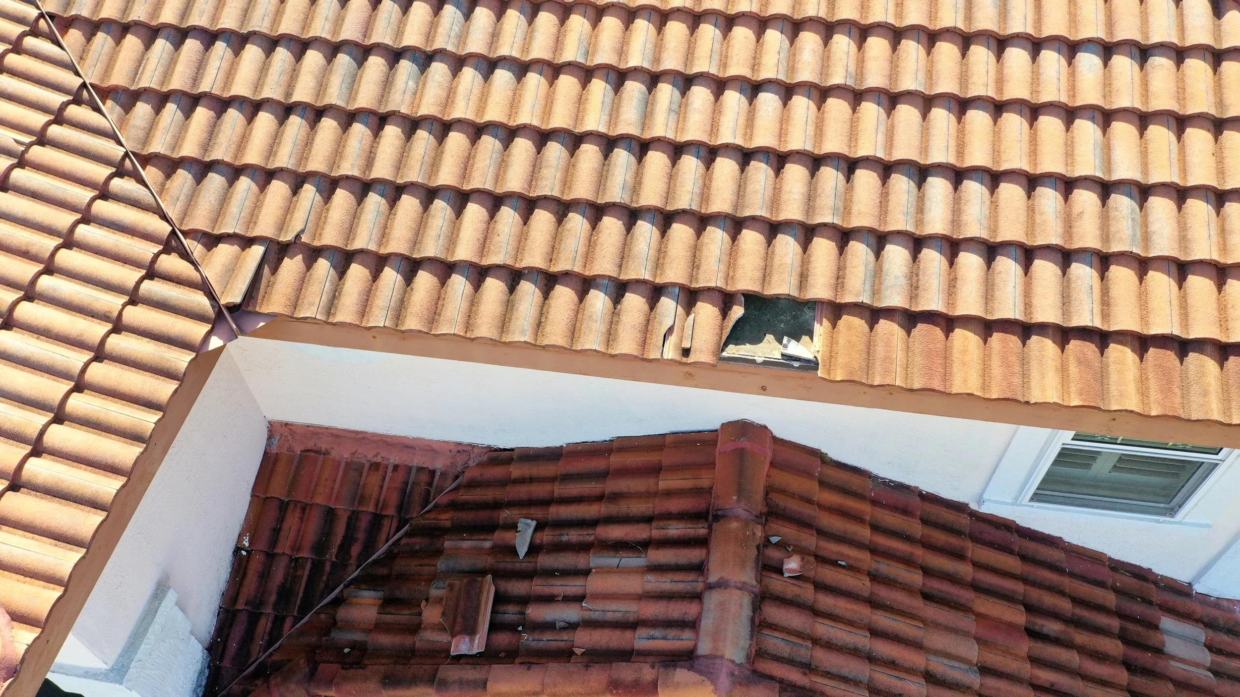 Hurricane-damaged concrete tile roof where displaced tiles fell and compromised the roofing layers beneath, exposing underlayment and decking to water intrusion. This type of cascading damage shows why loose or uplifted tiles must be addressed quickl