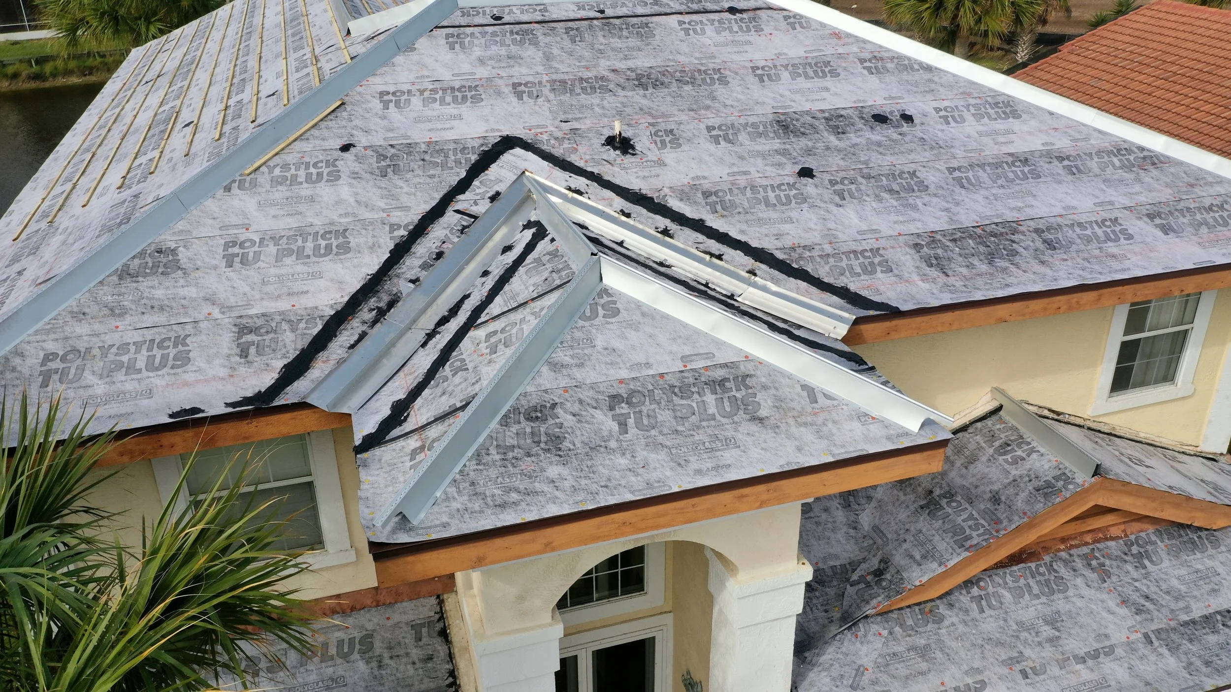 Concrete tile roof in preparation stage, clearly showing installed valley metals and ridge channels before final tile placement. These components create controlled water paths, protect critical transitions, and provide secure anchoring points — the s