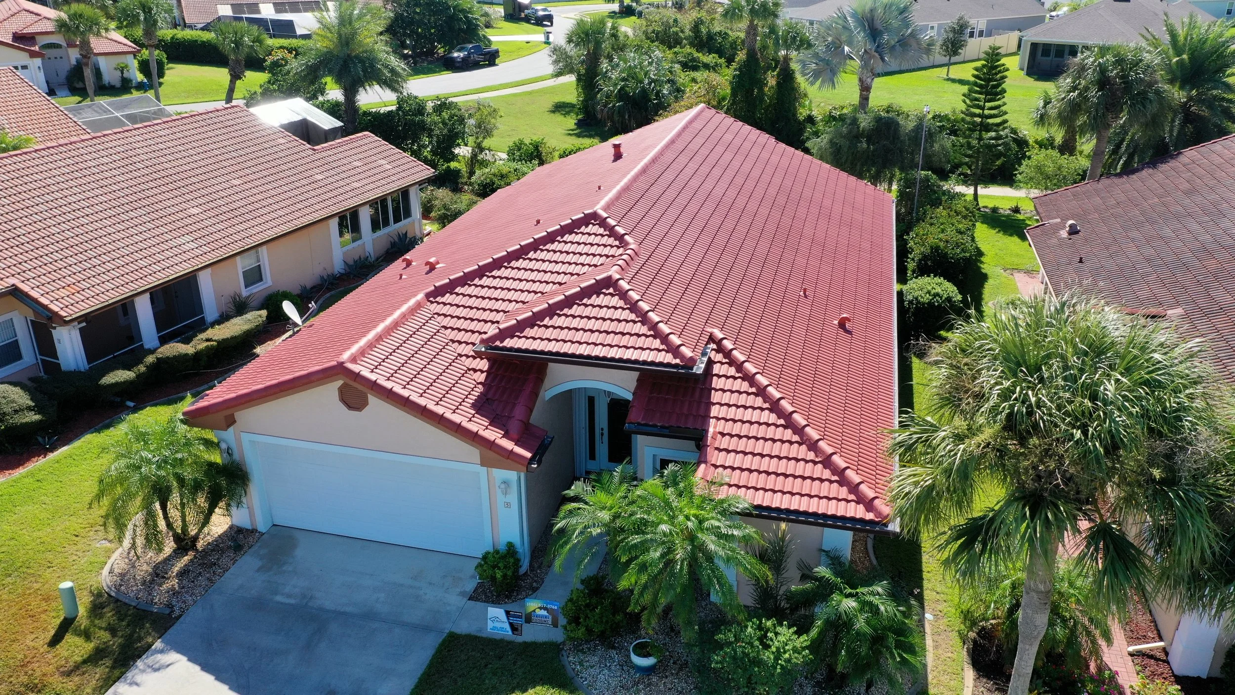 Aerial view of a single-family home with a red-tiled roof, surrounded by landscaped yard with palm trees and neighboring houses.