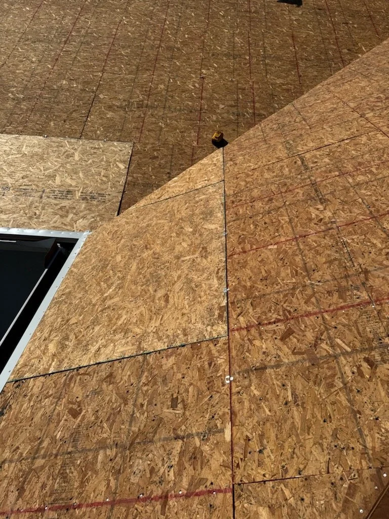 Exposed OSB plywood decking across multiple roof planes, showing crisp edges, consistent panel layout, and clear fastening lines. This modern decking provides a stable, uniform surface that supports accurate shingle alignment, reliable nailing, and i