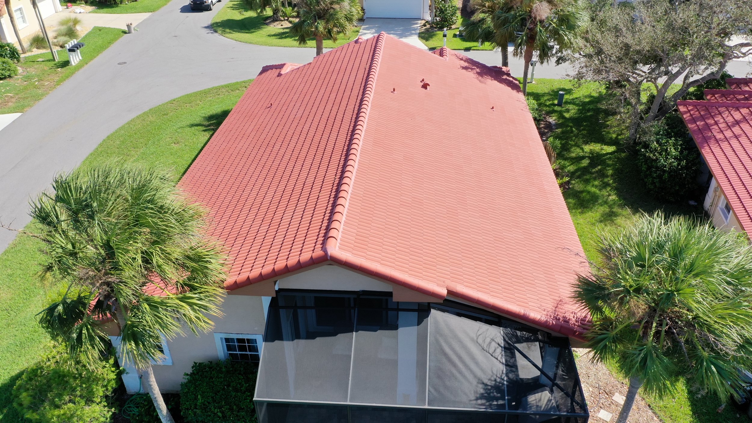 Aerial view of a house with a red tiled roof, surrounded by palm trees, green grass, and a driveway.