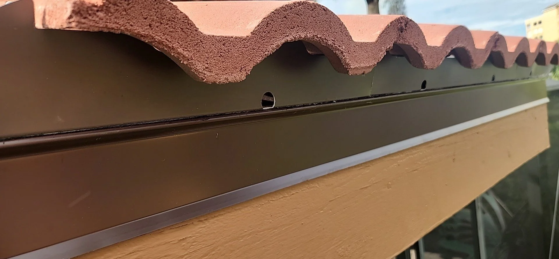 Close-up of a roofing eave with clay tiles and a metal drip edge installed on a wooden soffit.