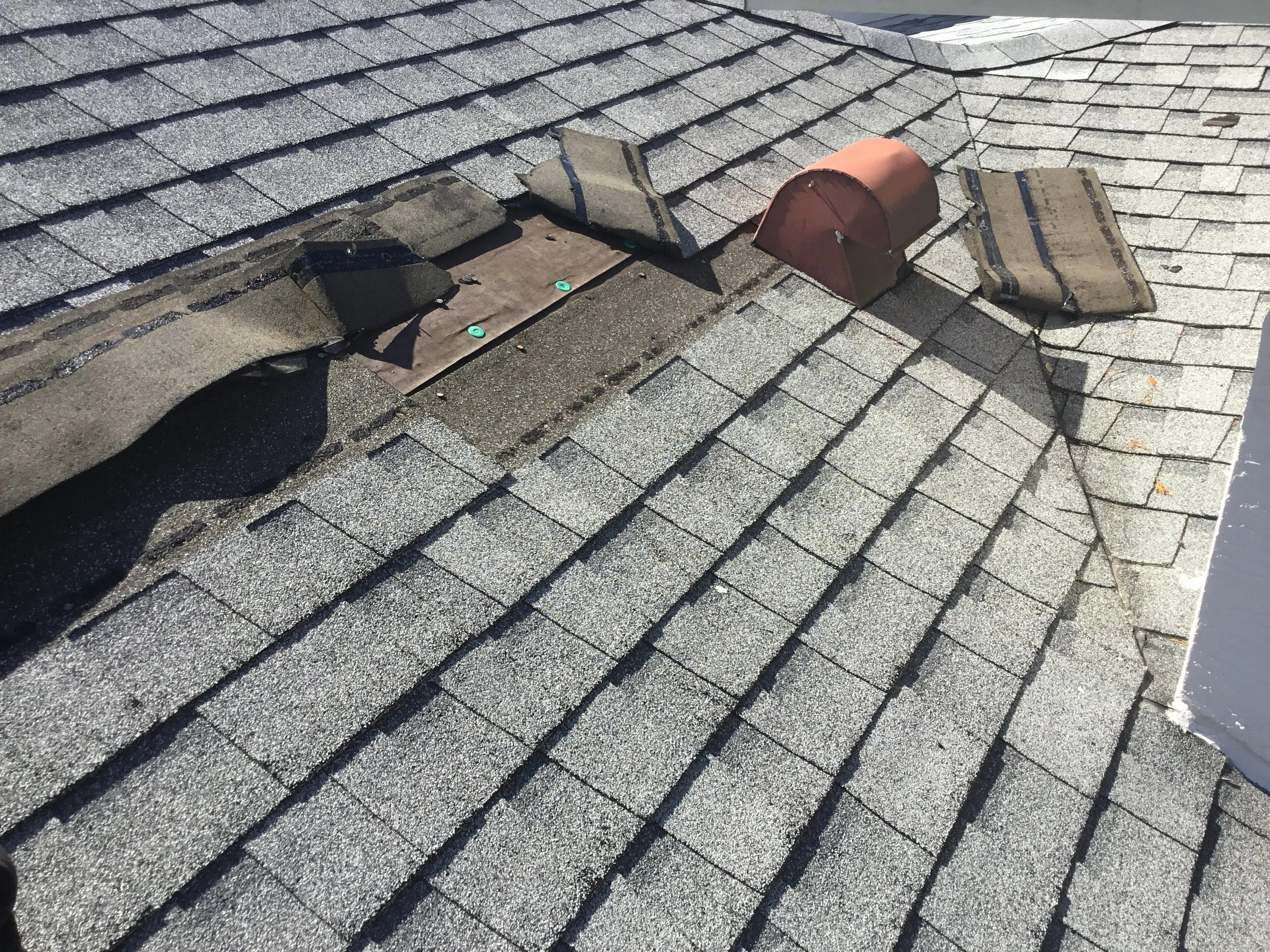 Asphalt shingle roof showing shingles blown off during a severe storm, leaving underlayment and decking exposed to wind-driven rain. Missing shingles create immediate leak risk and often signal the need for targeted repair or full replacement dependi