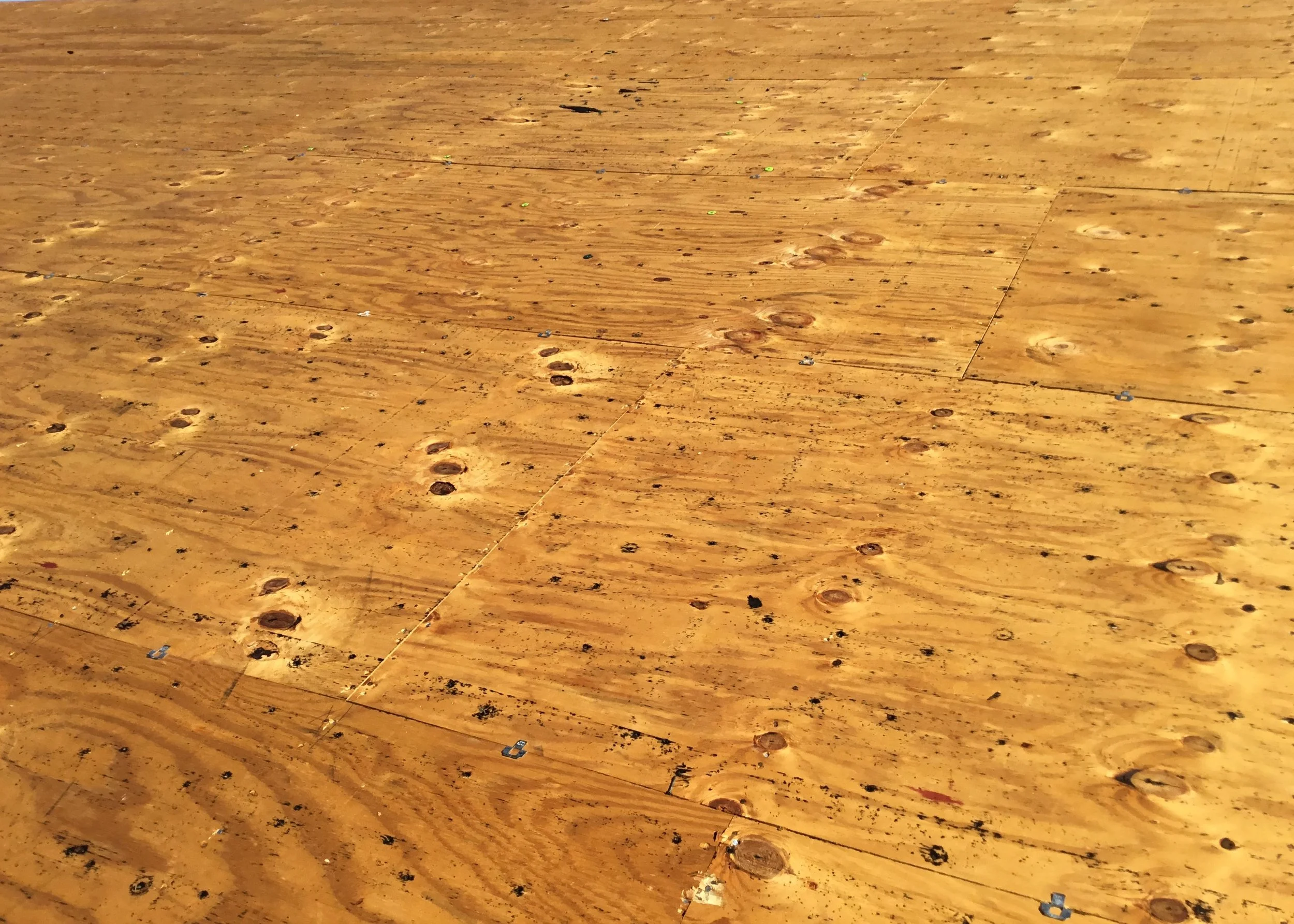 Roof decking fully exposed after tear-off, revealing bare plywood sheathing before new materials are installed. This stage allows for detailed inspection, damaged board replacement, and proper fastening by re-nailing the plywood to meet current state