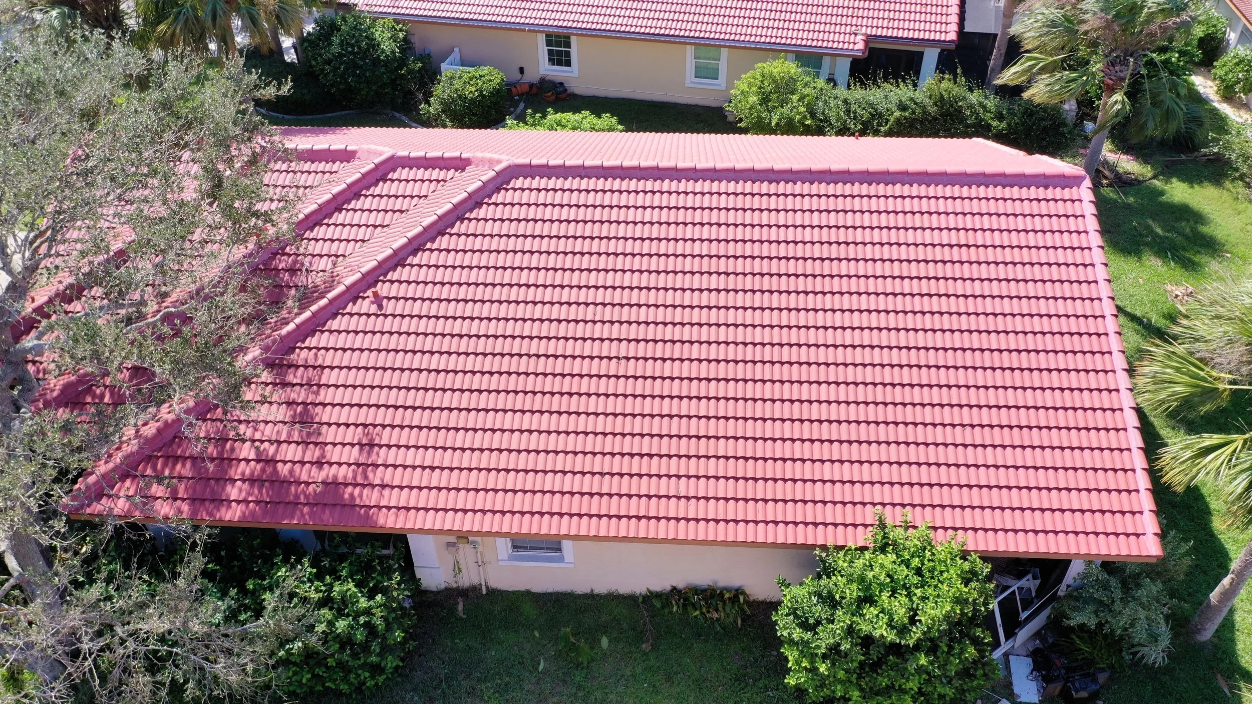Aerial view of a house with a red tiled roof, surrounded by green trees, bushes, and a lawn.