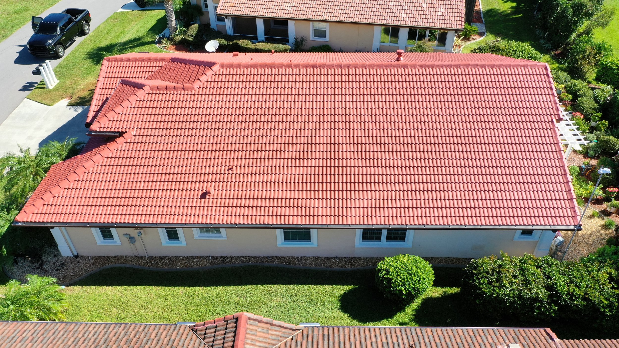 Aerial view of a house with a red tiled roof, surrounded by a green lawn, trees, and neighboring houses.
