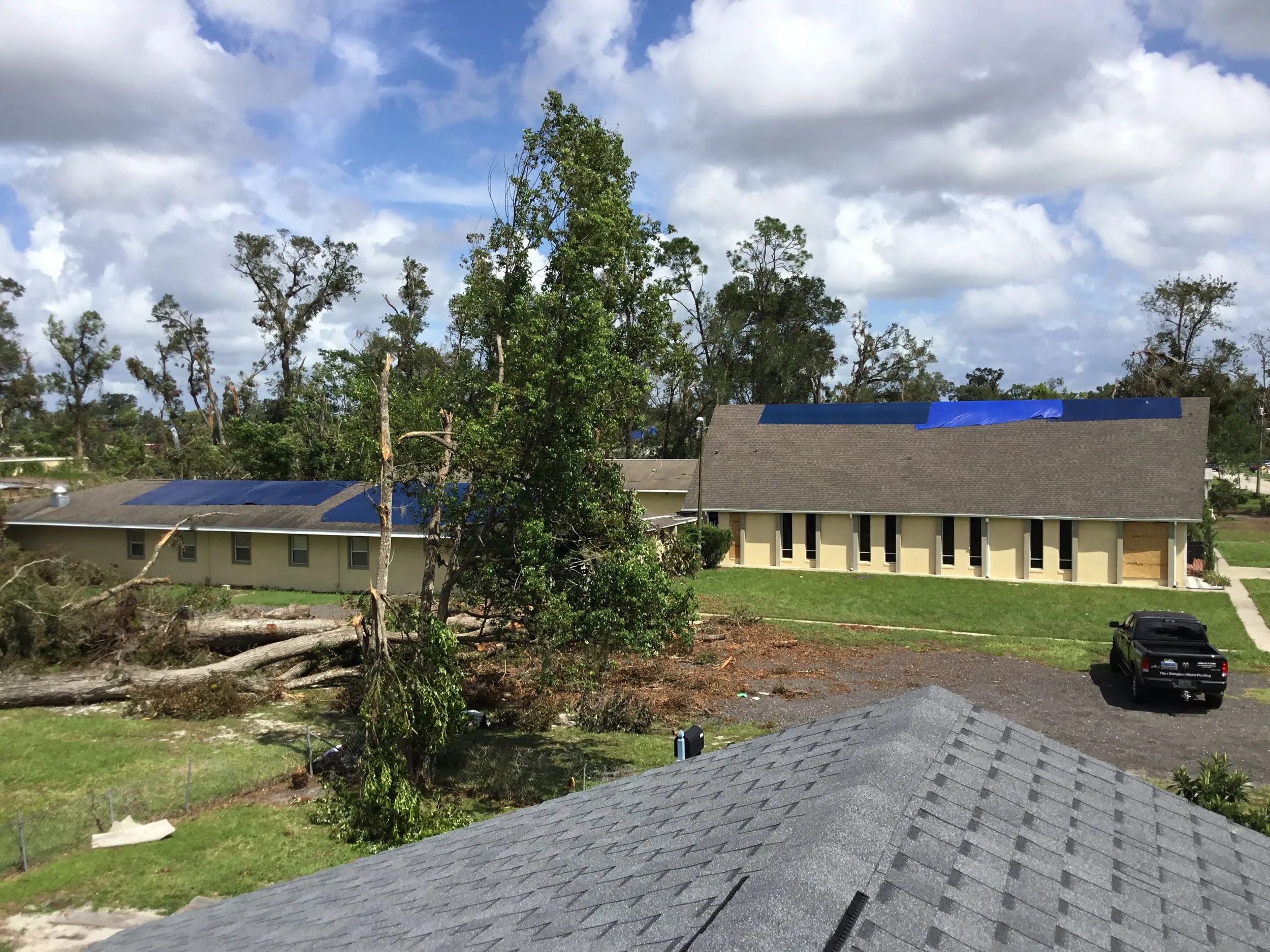 Tornado damage to an asphalt shingle roof where extreme winds stripped shingles from multiple planes and scattered debris across the property. Damage of this scale requires full tear-off and rebuild with upgraded underlayment, reinforced fastening pa