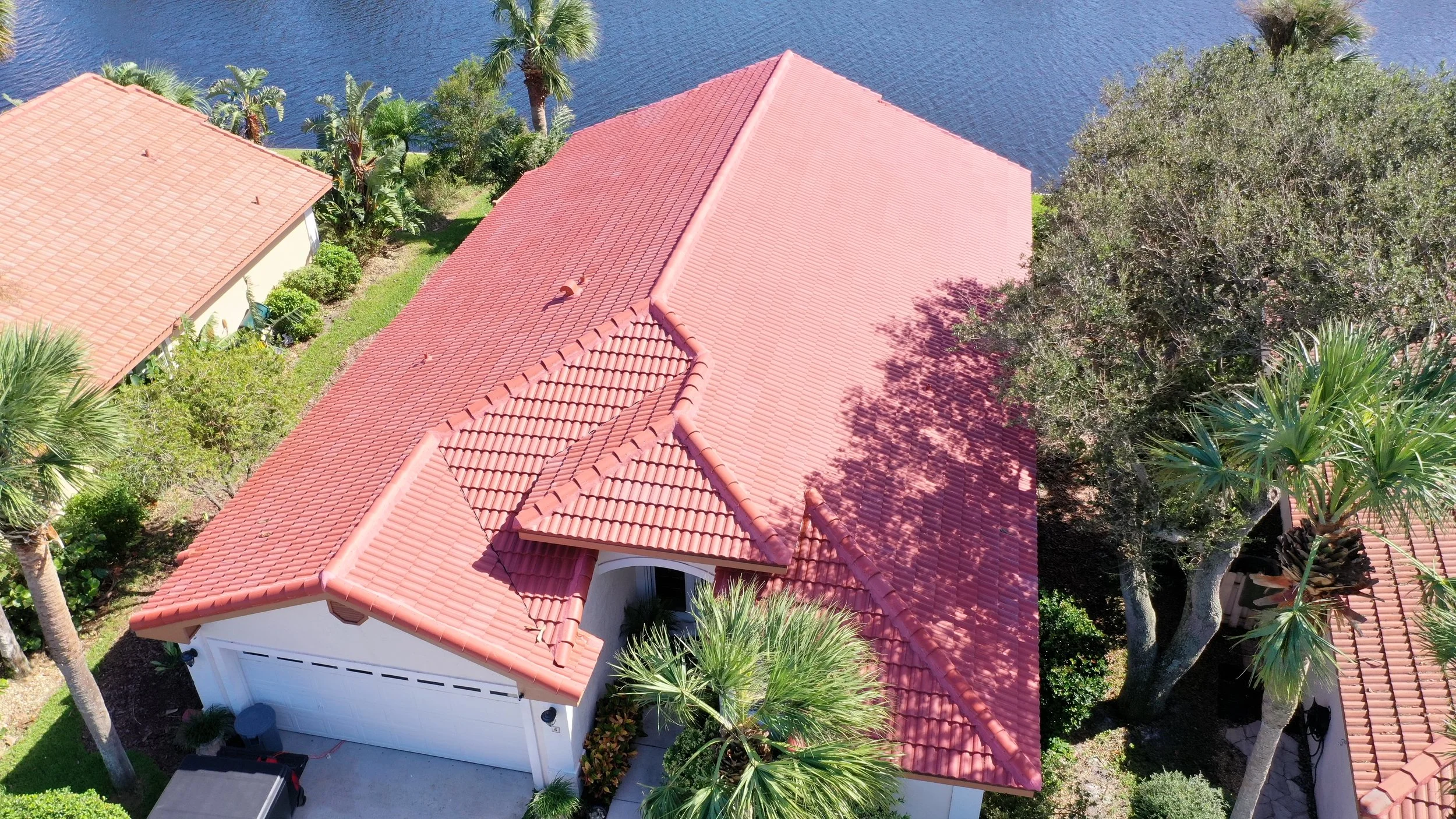 Aerial view of a house with a red-tiled roof, surrounded by green trees and near a body of water.