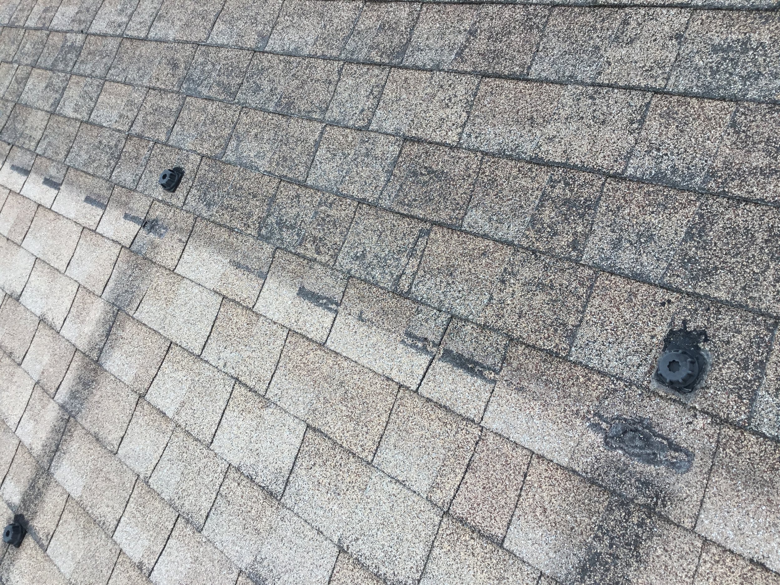 Asphalt shingles revealed after a pool heater was removed, clearly showing the contrast between sun-exposed shingles and those that were protected for years. The covered area retains deeper color and granules, while surrounding shingles show weatheri