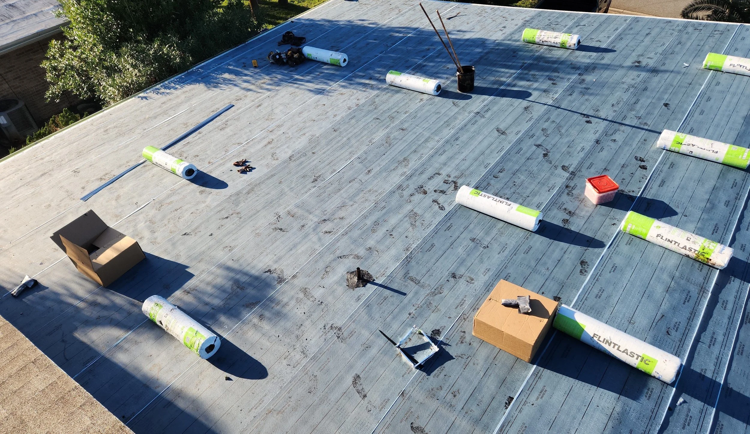 Flat roof base sheet laid out with membrane rolls precisely aligned and staged for cap-sheet installation. This organized setup ensures clean seams, consistent overlap, and reliable heat welding — critical steps in building a durable, leak-resistant 