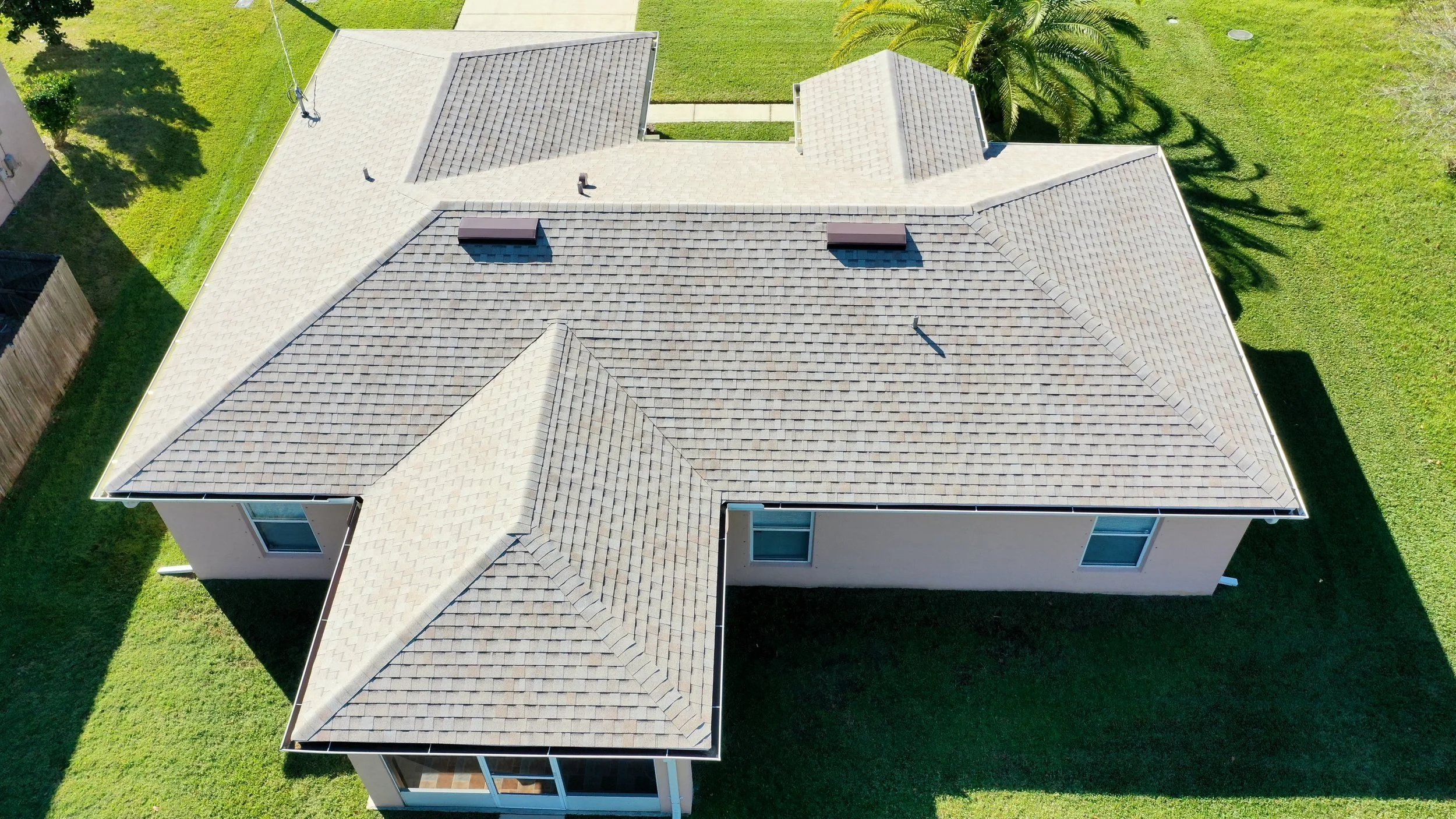 An aerial view of a house with a multi-gabled roof, surrounded by grassy yard and trees.