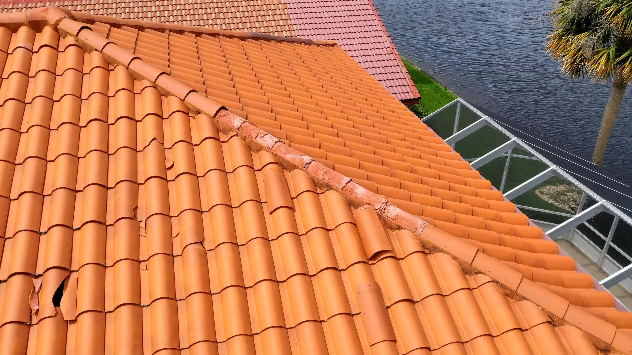 Clay tile roof showing hurricane damage along the hip caps, where uplift and lateral wind forces displaced and cracked tiles at critical transition points. Hip caps are especially vulnerable in high-wind events when fastening or mortar systems are in