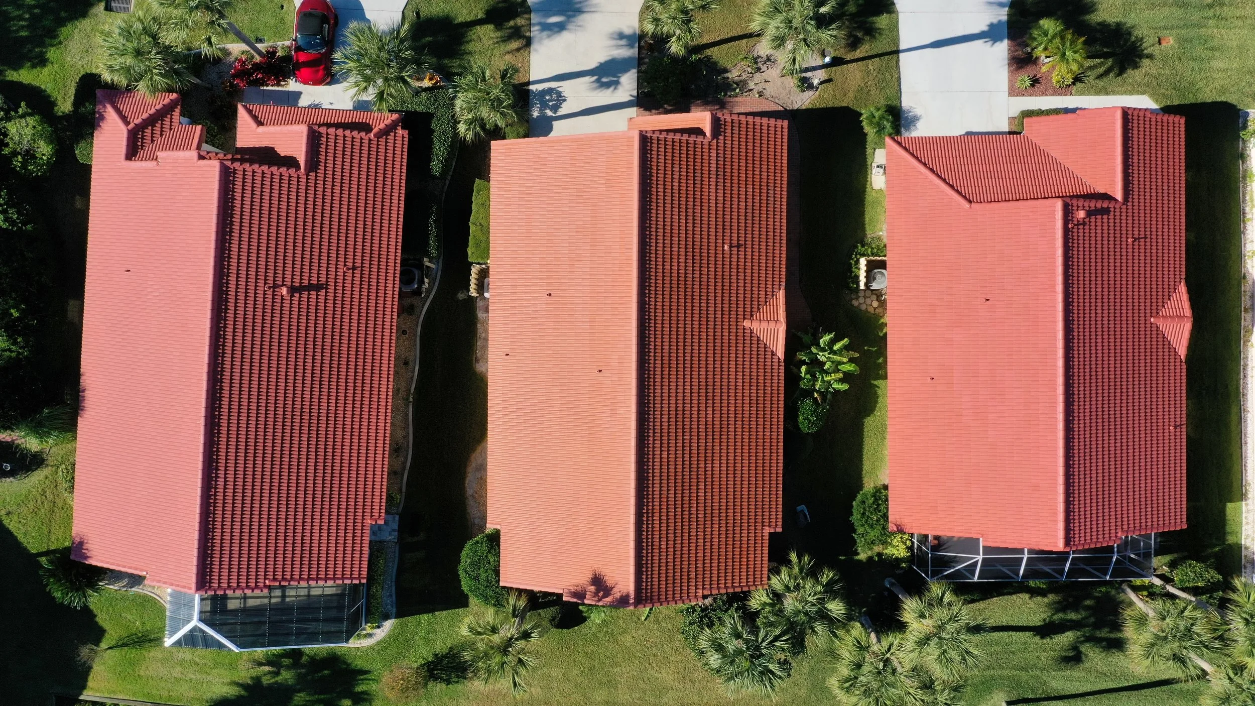 Three houses with red tile roofs viewed from above, with palm trees and green lawns in the yards.