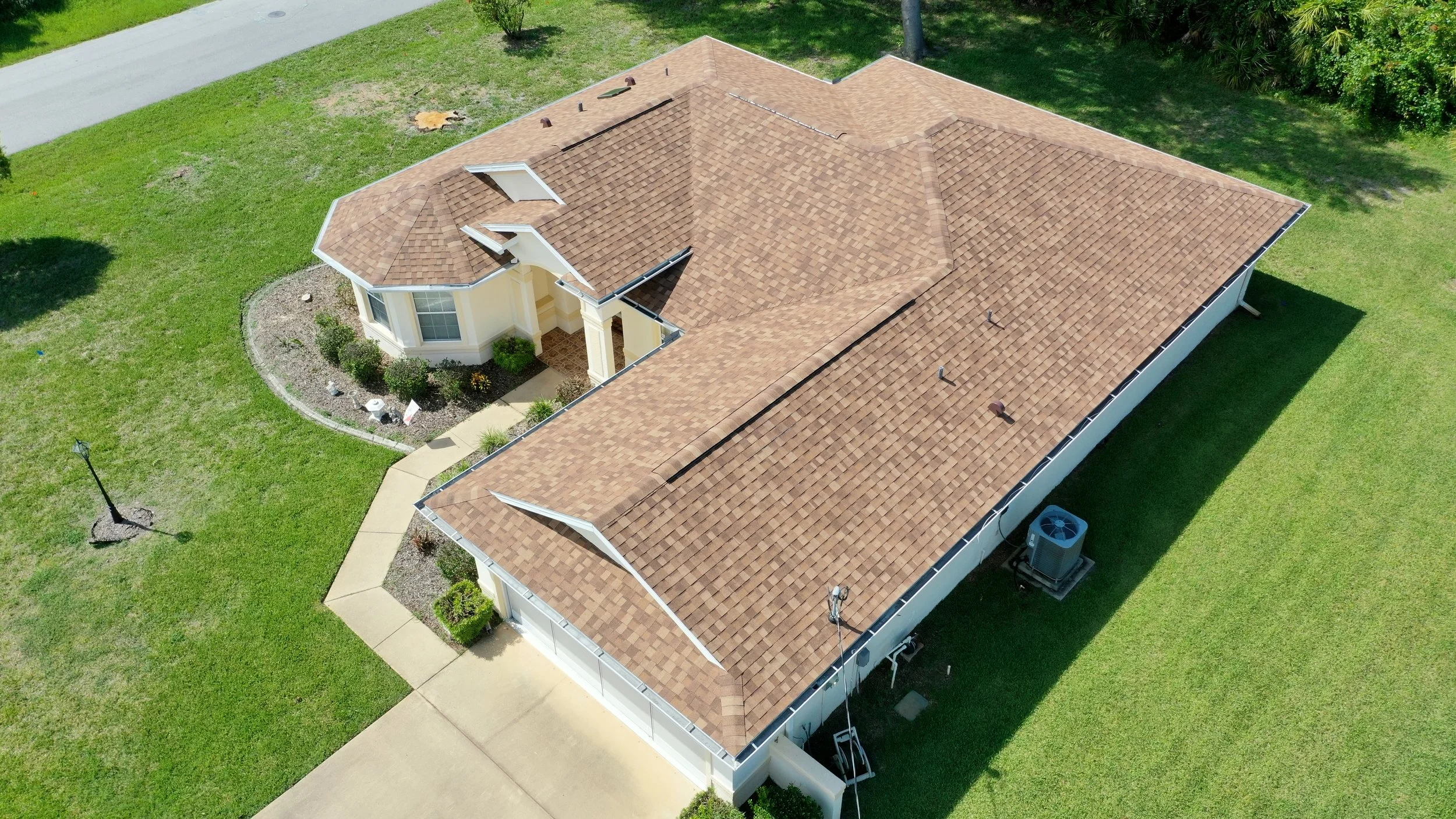 Aerial view of a house with a brown shingle roof, surrounded by green lawn and vegetation.
