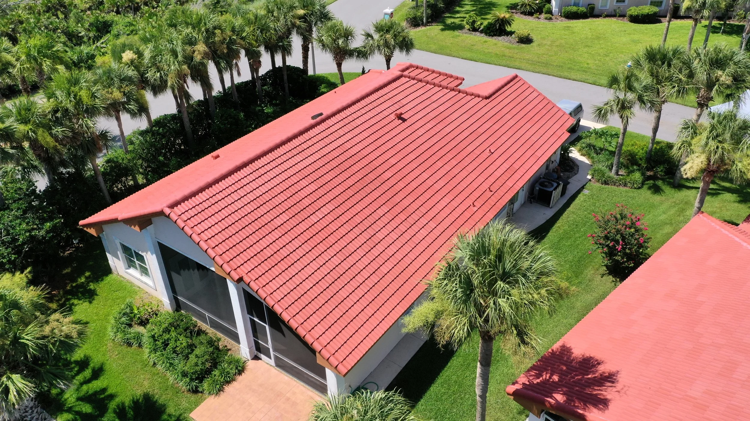 Aerial view of a house with a red tiled roof surrounded by palm trees and green lawn.