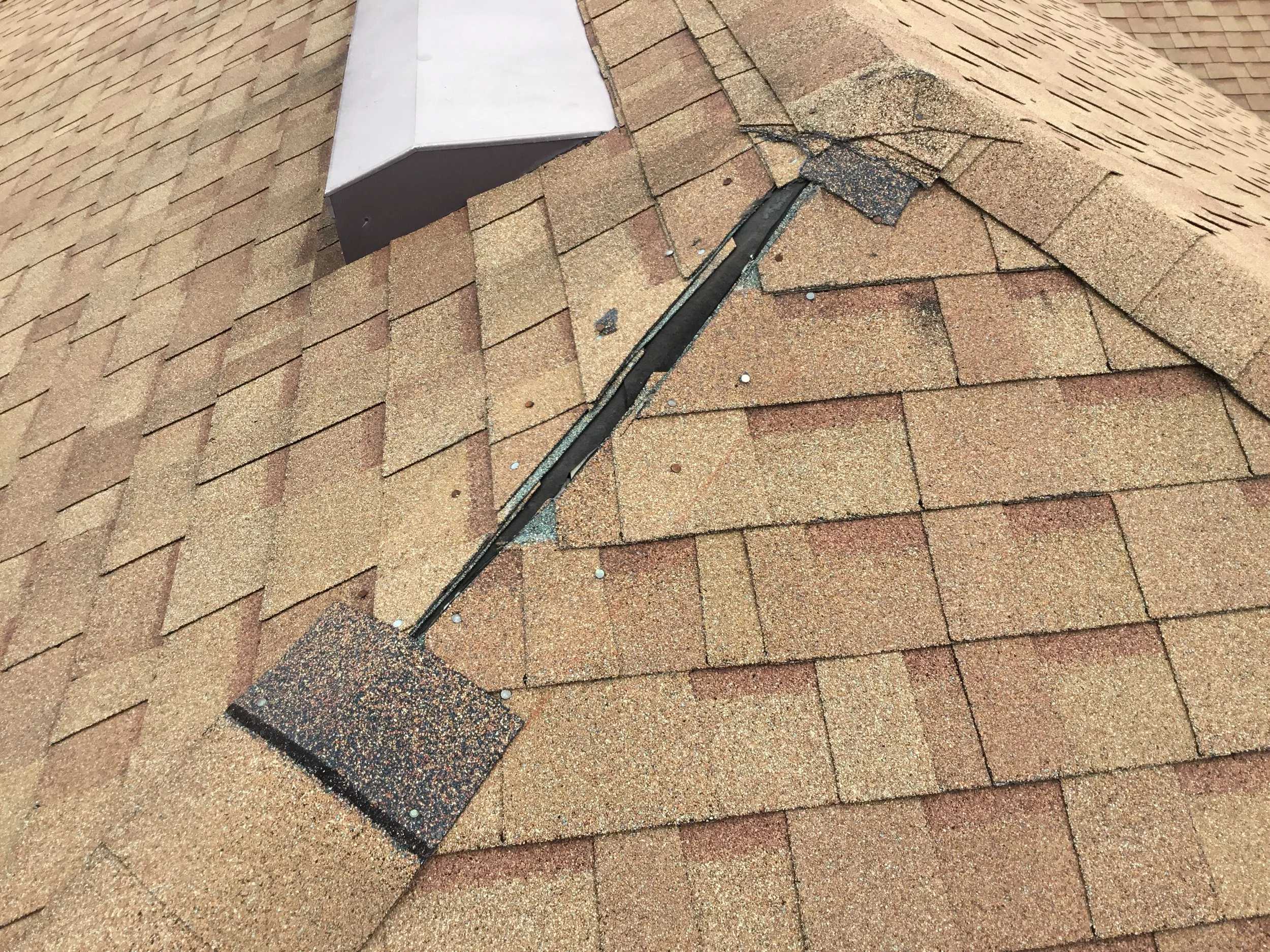 Storm damage on a single asphalt shingle roof where hip caps were blown off, leaving the underlying ridge and decking vulnerable to wind-driven rain. Once hip protection is lost, water can track down the peak and into multiple roof planes — which is 