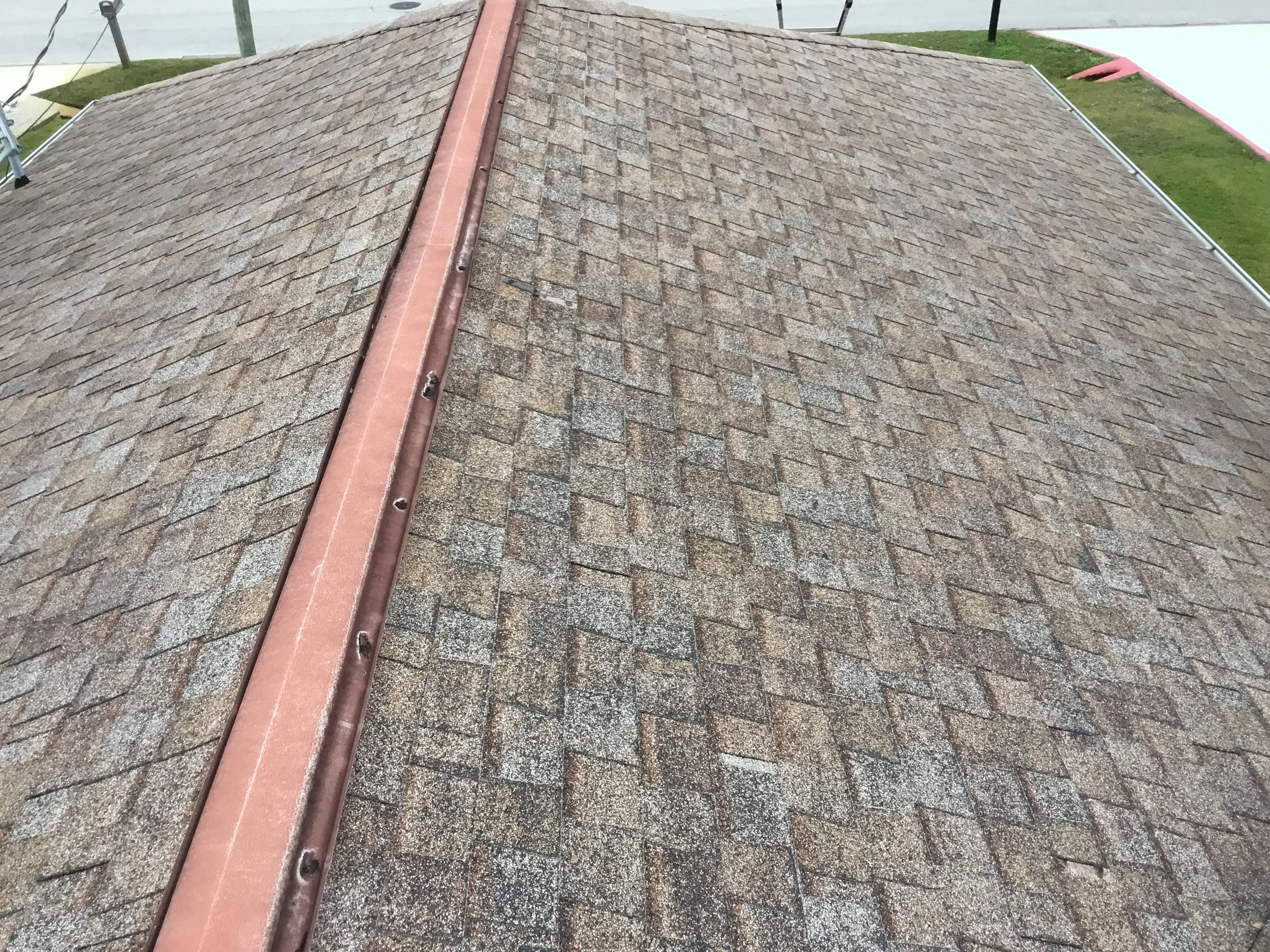 Aged asphalt shingle ridge showing severe granule loss, where bare fiberglass matting and surface wear indicate advanced deterioration. Once granules are this depleted, shingles no longer effectively protect against UV damage, heat, or water intrusio