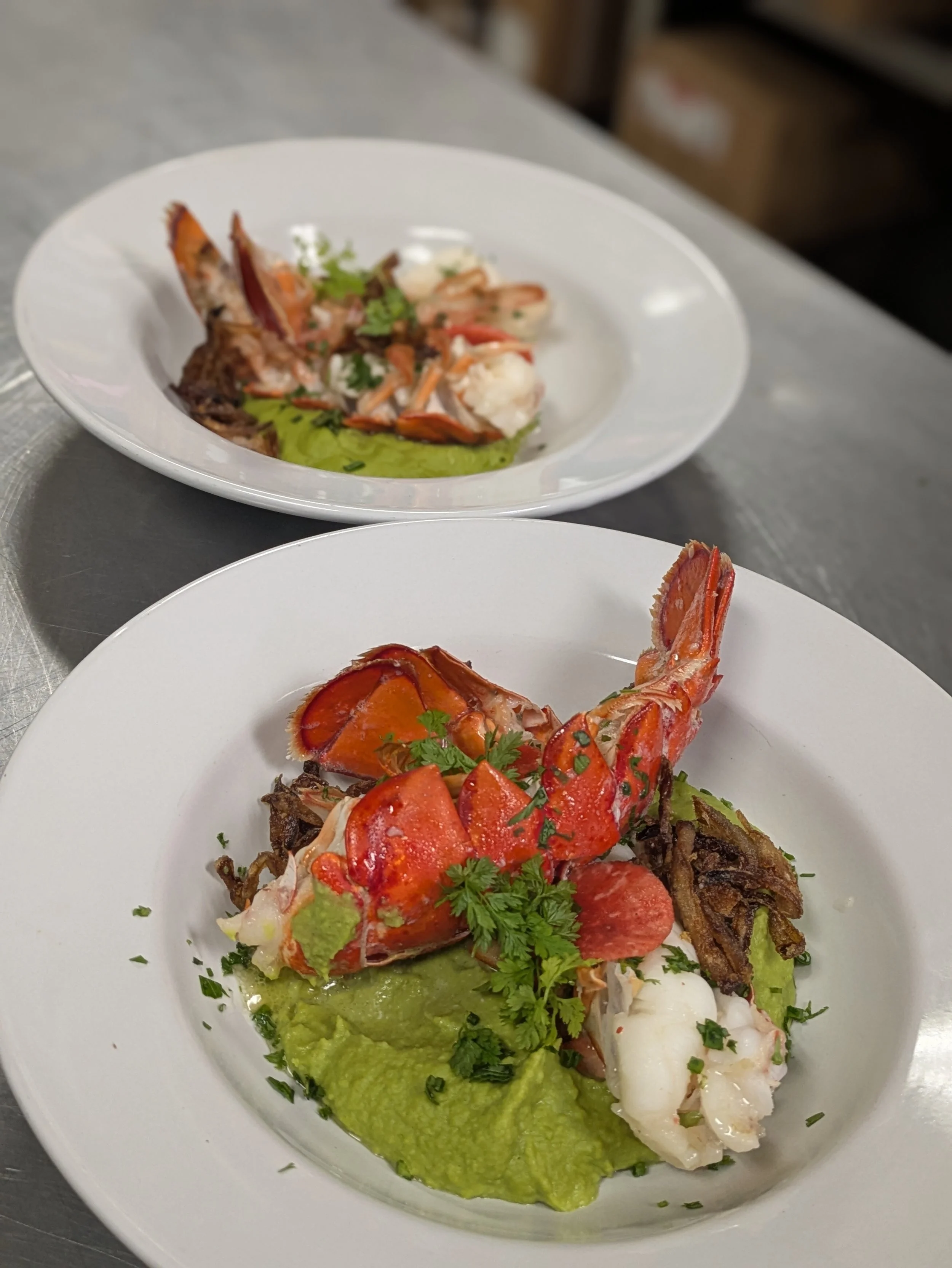 Lobster dish with green sauce, garnished with herbs, on a white plate.