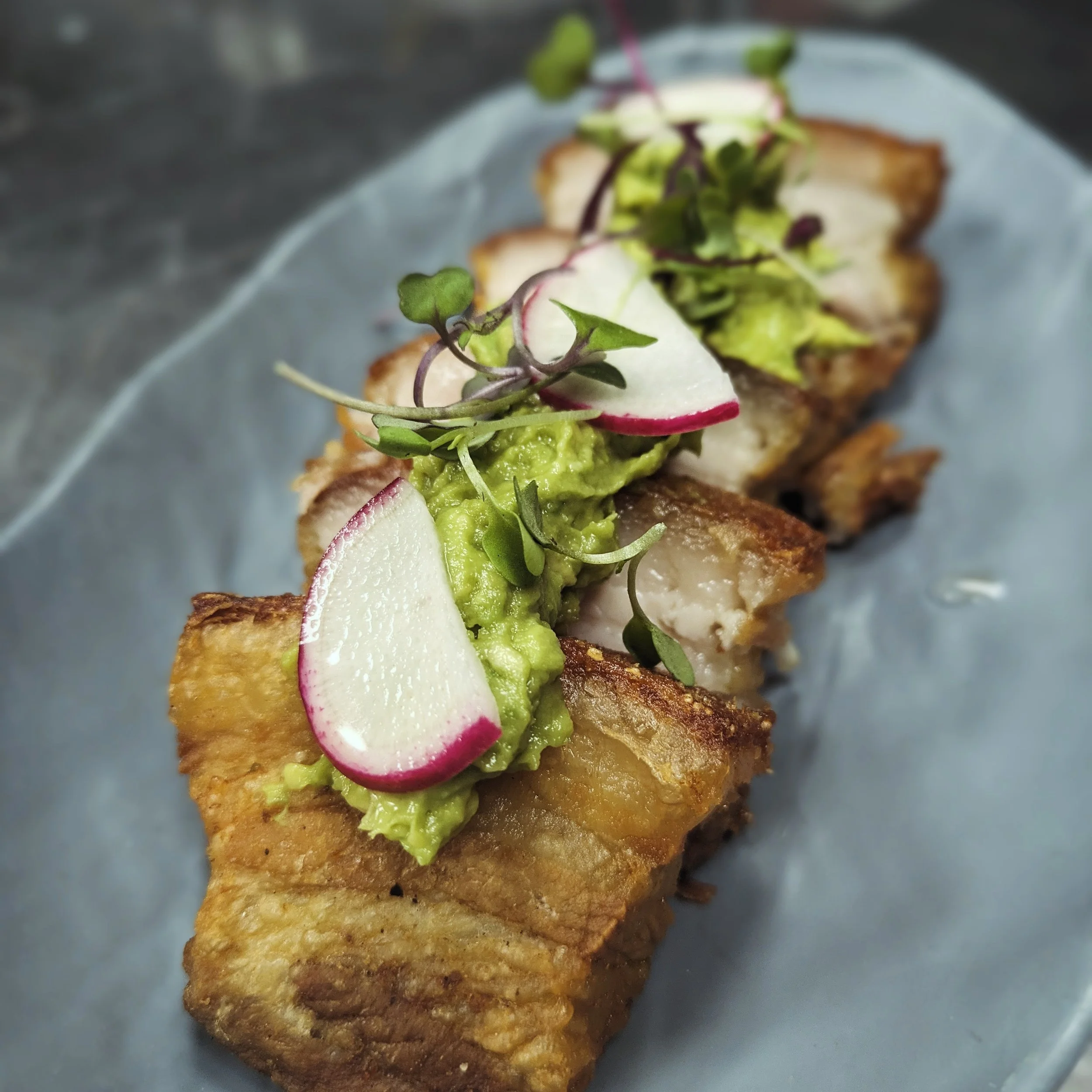 Fried fish topped with guacamole, sliced radishes, microgreens, and thinly sliced white onions on a plate.