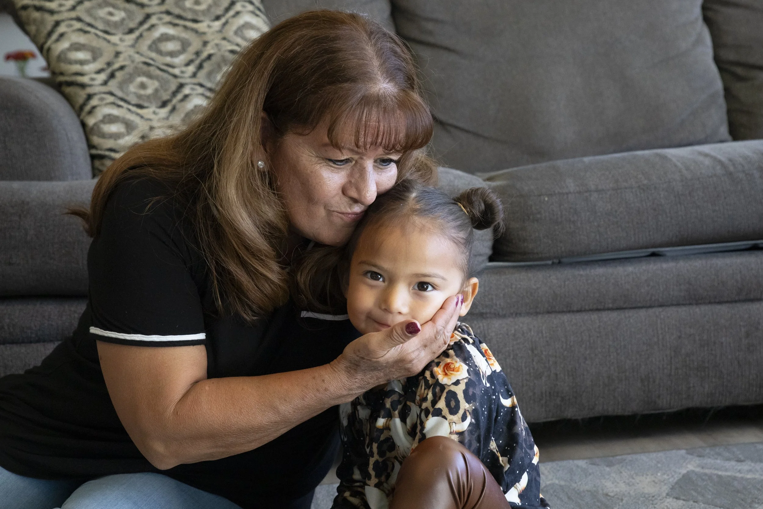 A woman cuddling a young girl with a gentle smile, indoors on a living room floor.