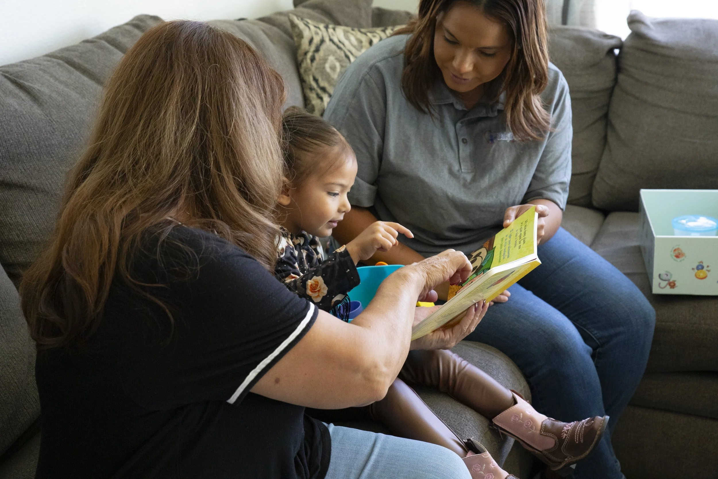 Three females, including a young girl, sitting on a sofa, looking at a children's book.