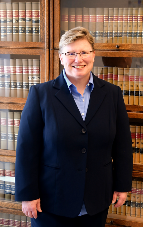 A smiling woman in a dark blue suit standing in front of a bookshelf filled with law books.