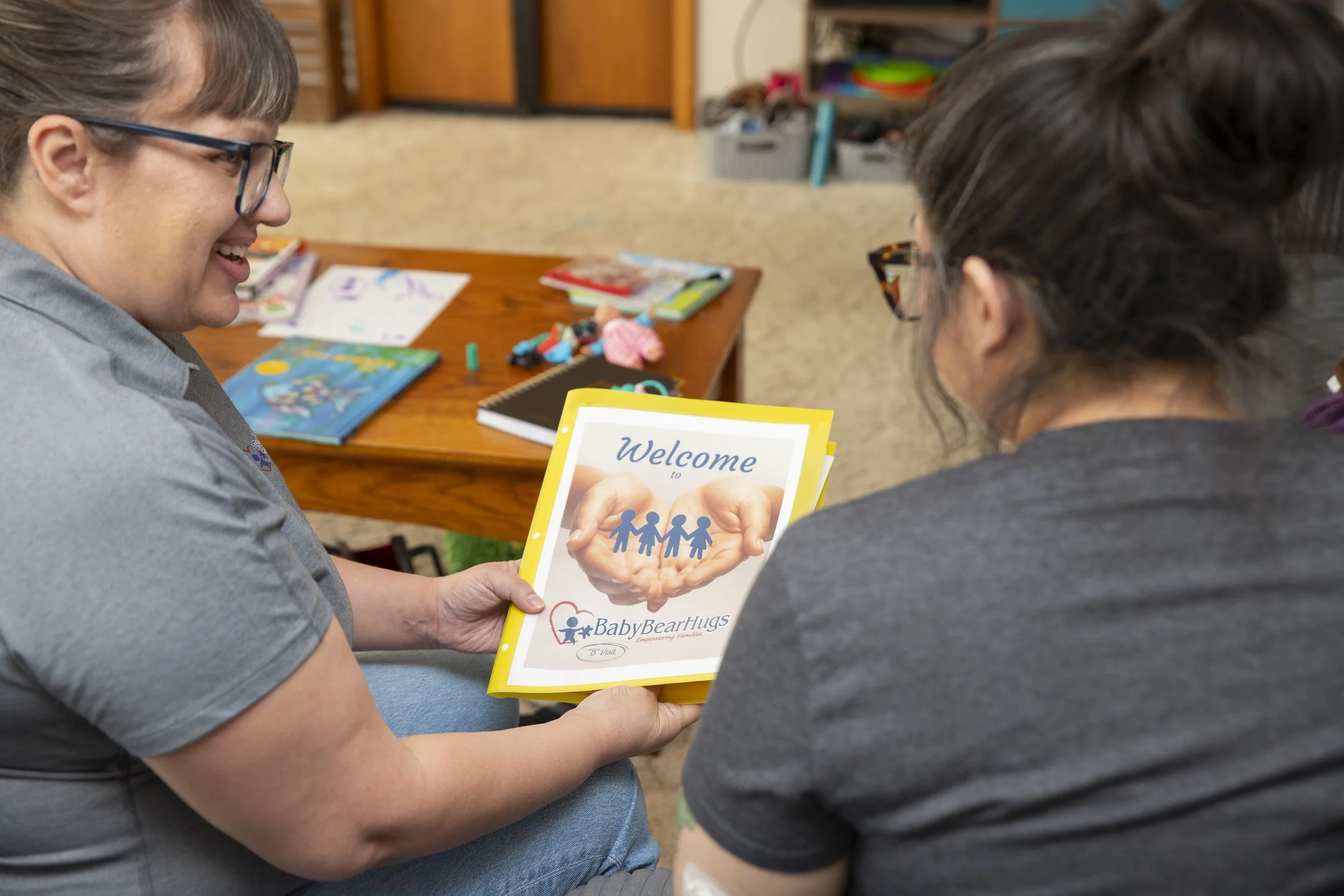 A woman holding a welcome booklet titled 'Baby Bear Hugs' with an image of hands holding paper cutouts of children.