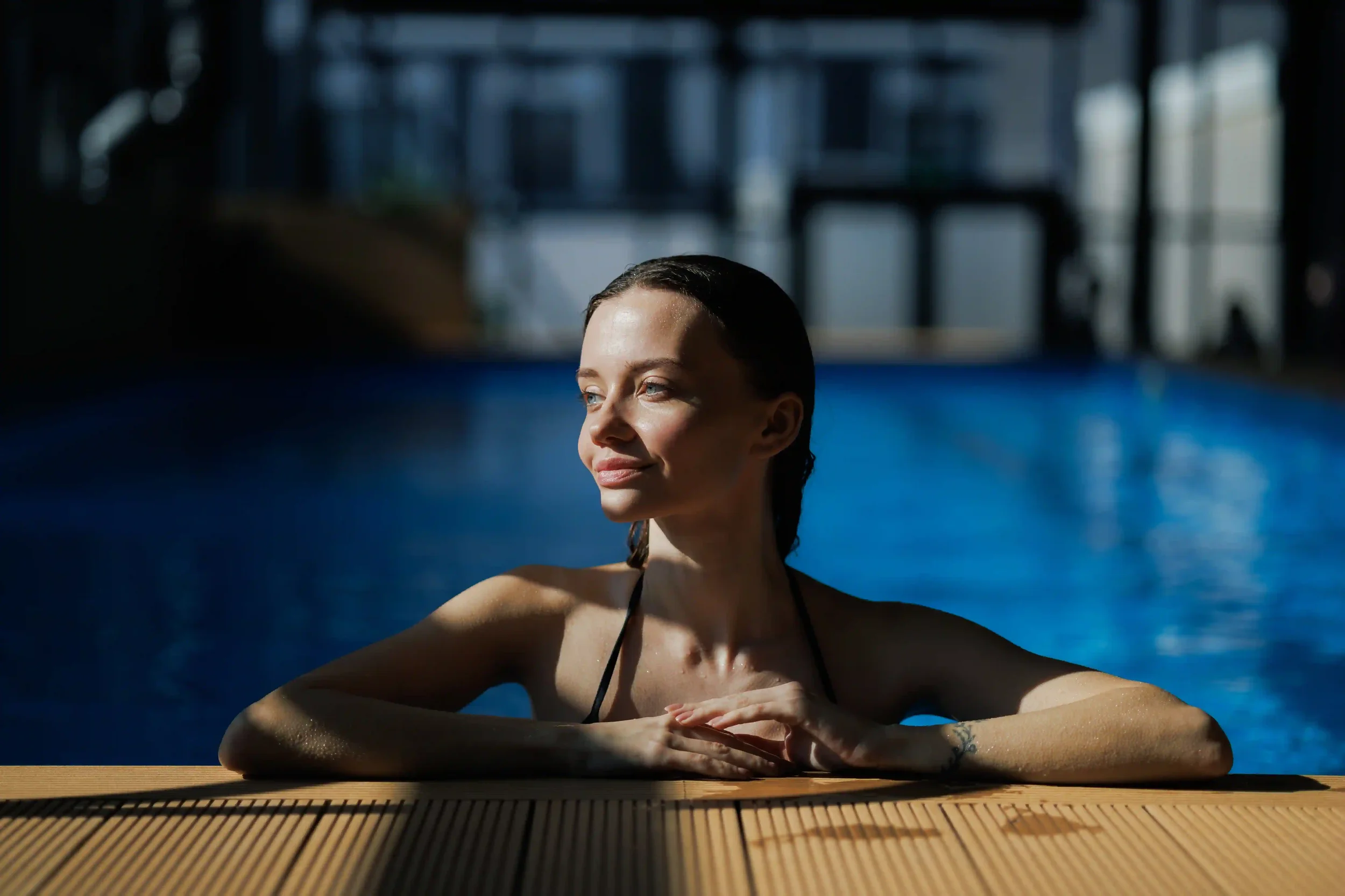 A woman relaxing in a swimming pool with sunlight on her face, leaning on the pool edge.