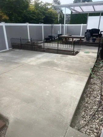 A backyard with a concrete patio, a fenced garden area with metal fencing, and a screened porch with outdoor furniture.