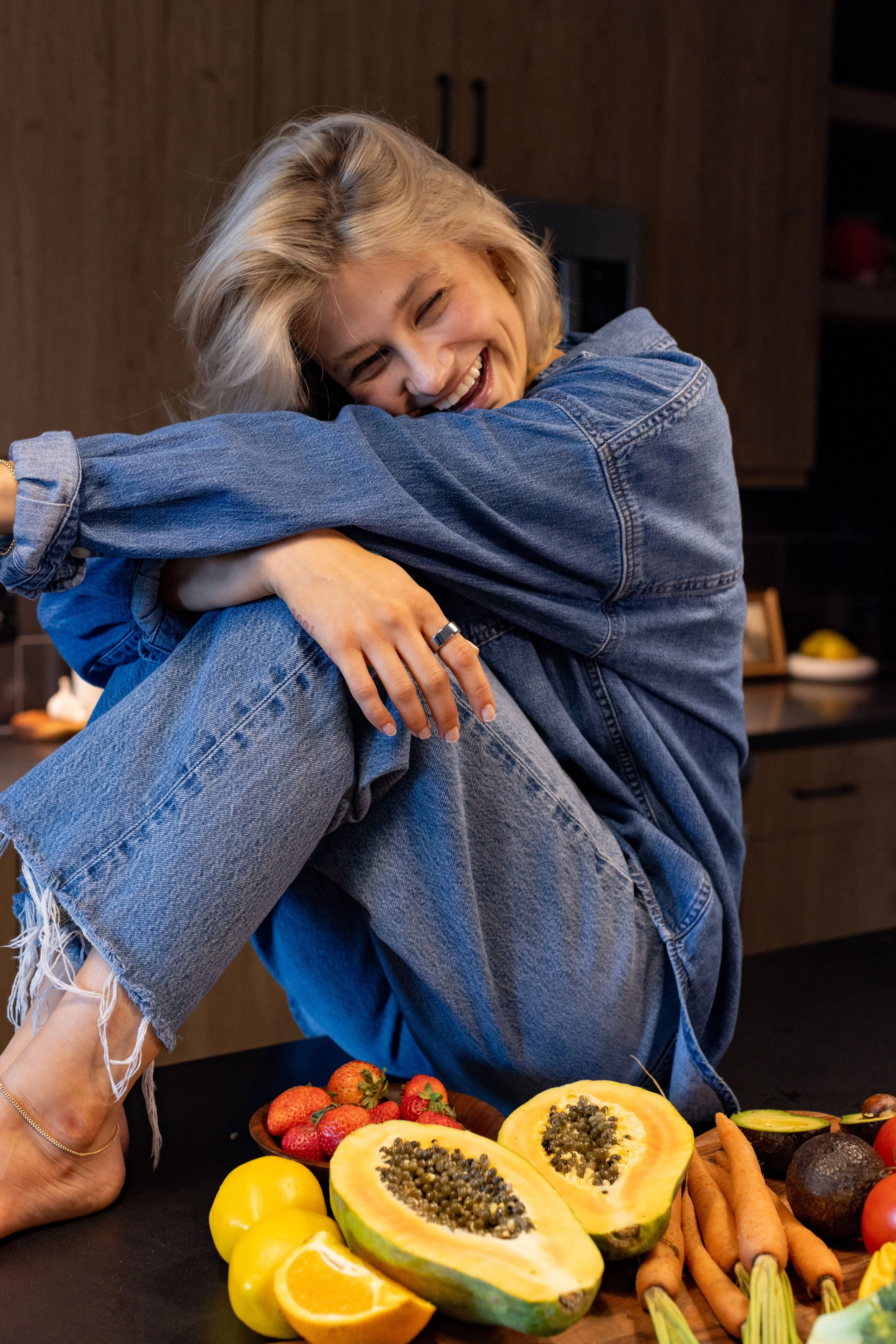 Carly Micek, founder of JOEY, sitting on the counter with fruits and vegetables smiling