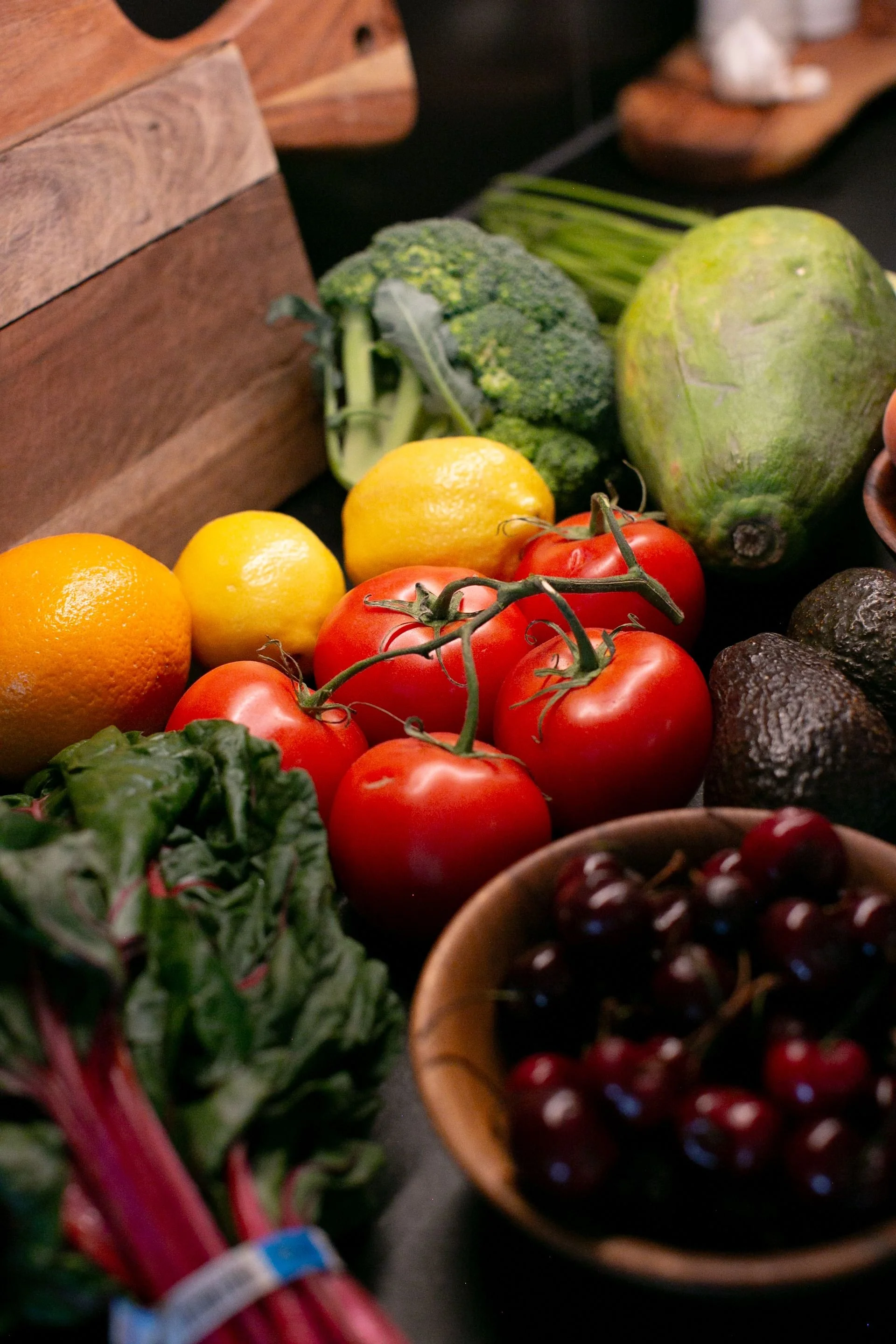 A spread of tomatos, avocados, lemons, papaya, and leafy greens on a cutting board
