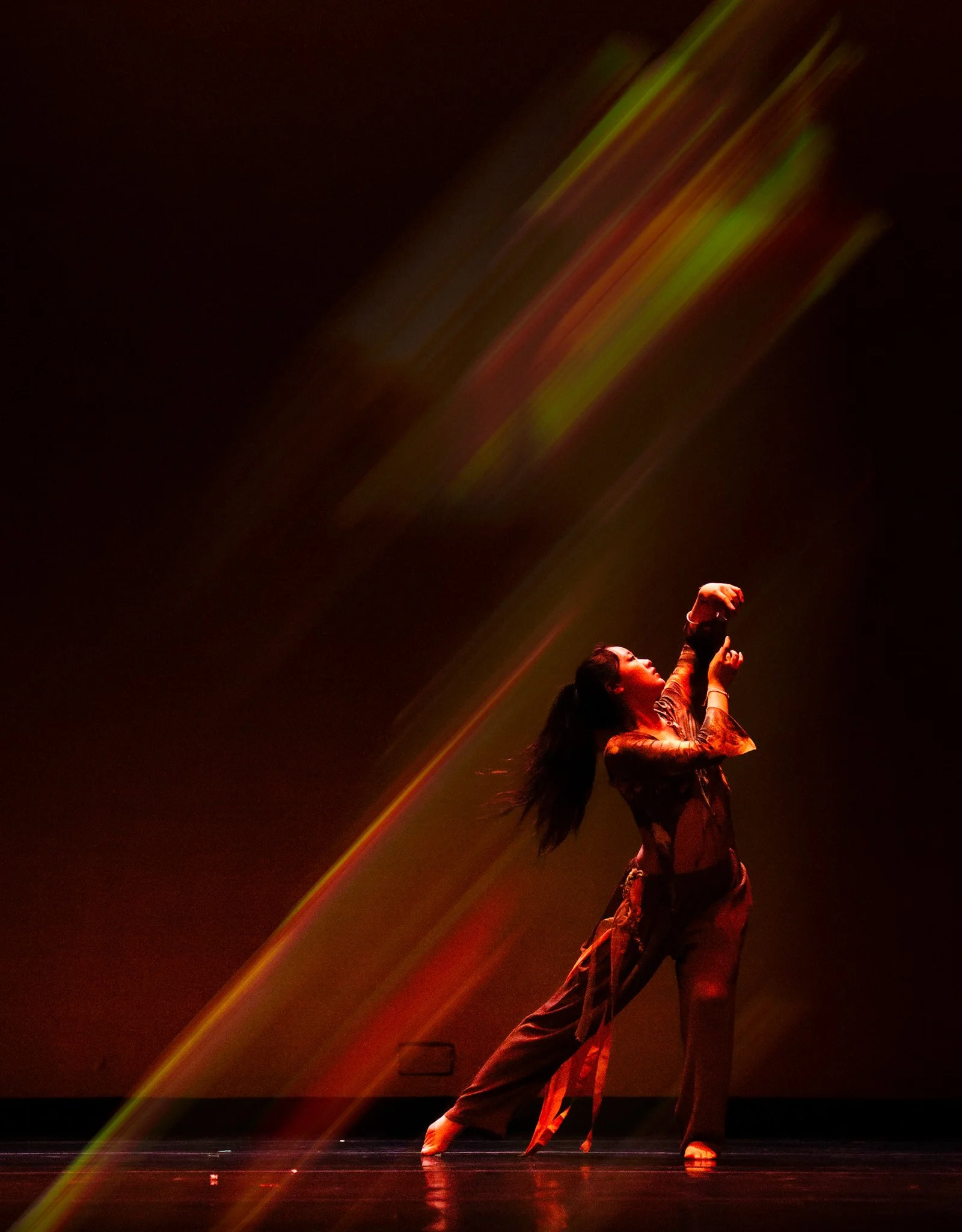 A dancer performs on stage with colorful streaks of light in the background.