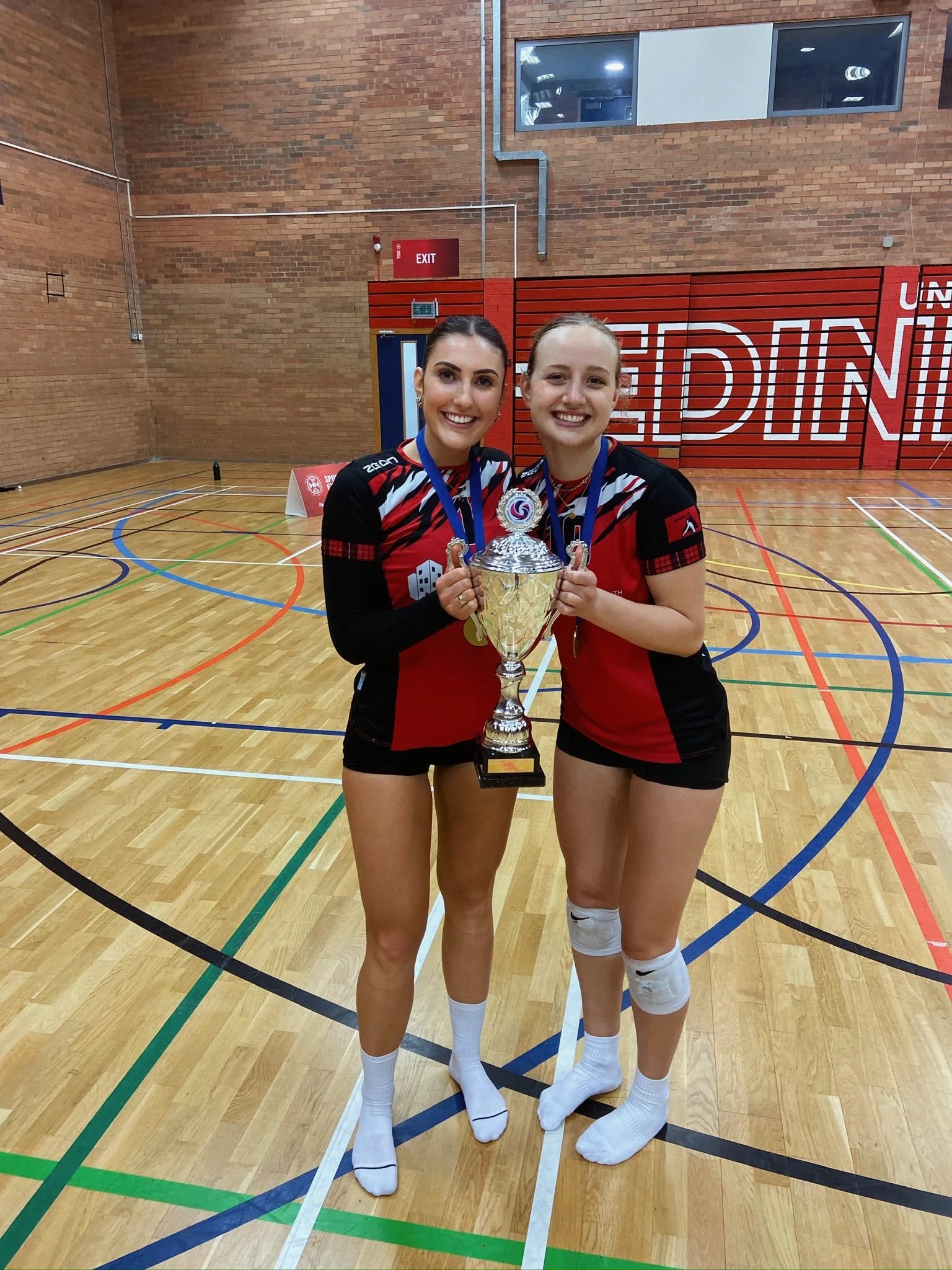 Maddy Weber posing with Scottish Volleyball teammate in red and blue kit inside indoor volleyball facility