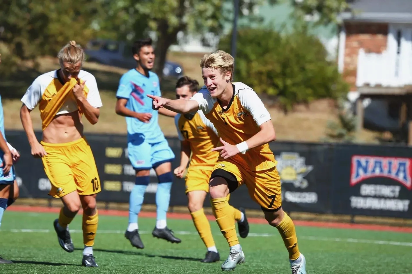 Alex Greive celebrating with Northern Kentucky University teammates in yellow and black striped jerseys during NCAA Division I match