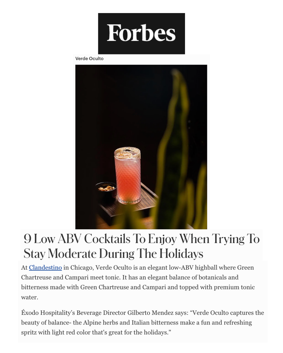 A pink cocktail in a tall, textured glass with a lemon twist garnish, set on a wooden surface with a black background and some blurred green leaves in the foreground.