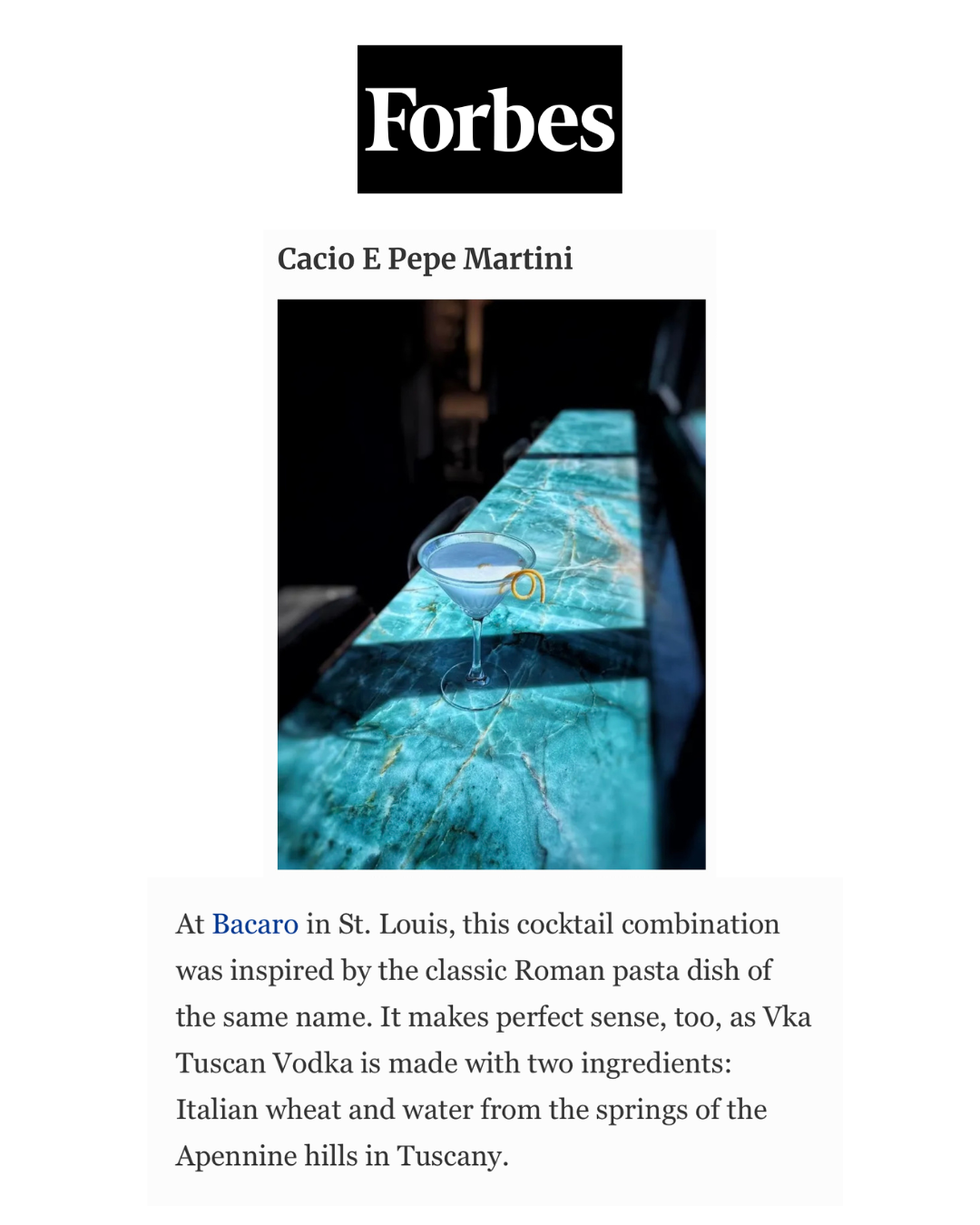 A cocktail glass with a lemon twist garnish placed on a polished green marble bar surface, with a blurred background.